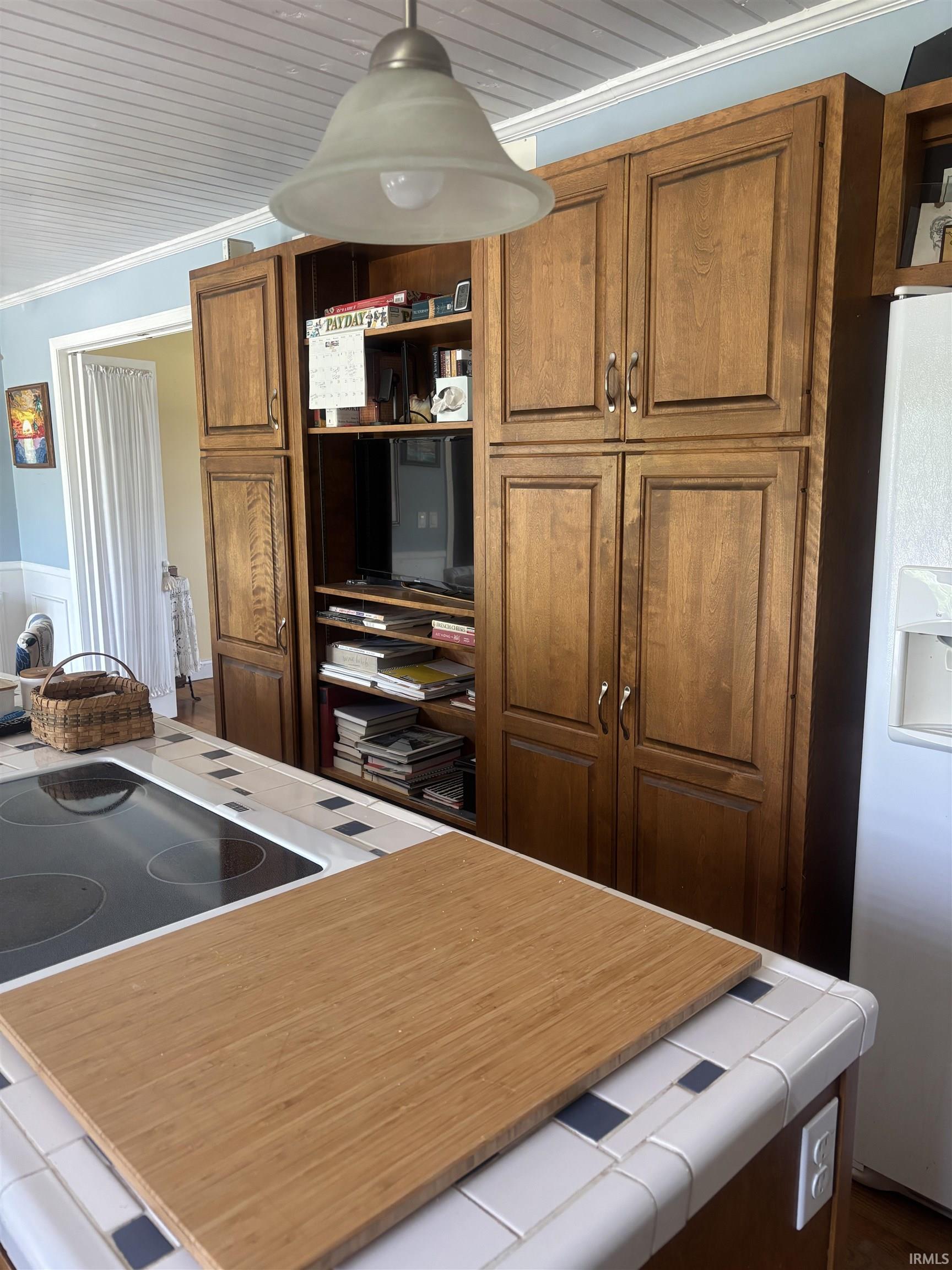 Custom built-in cabinetry with wood-finish doors and open shelving, integrated cooktop, tile countertop, beadboard ceiling, and pendant lighting