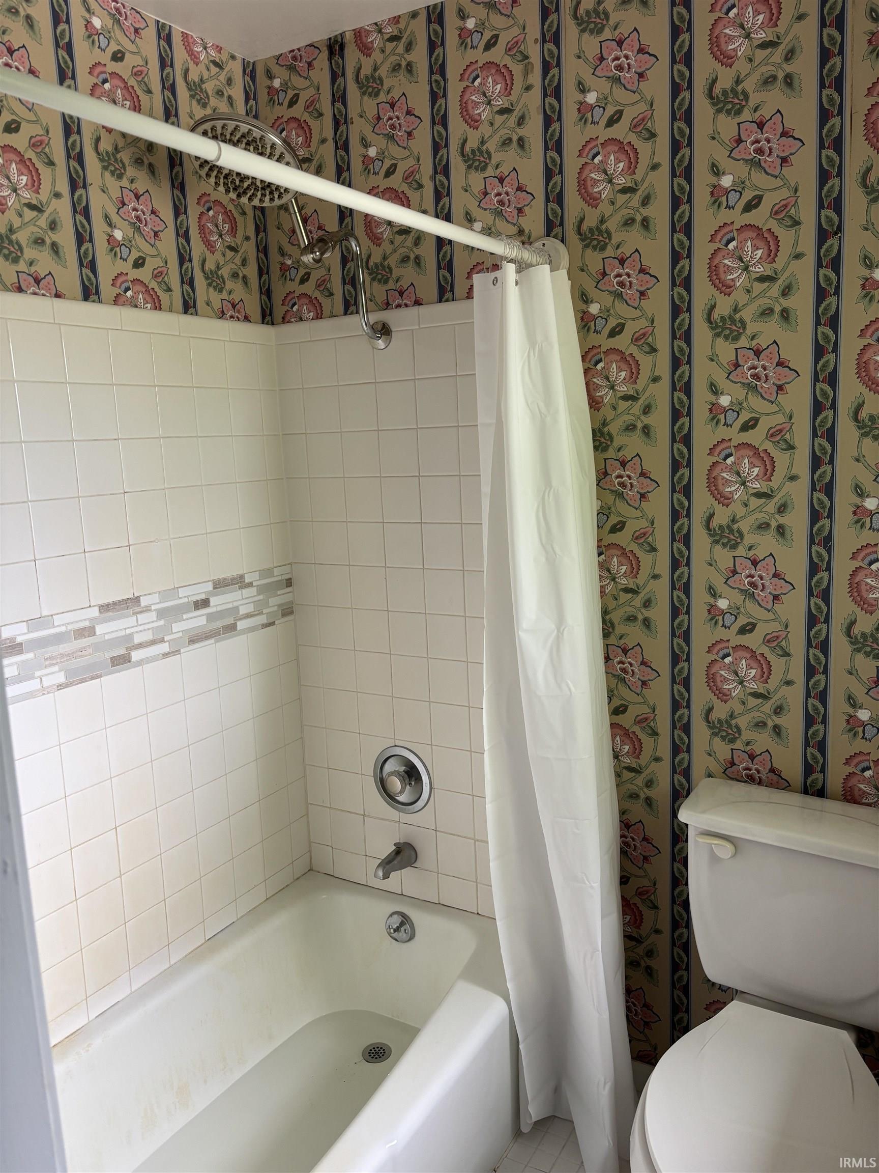 Bathtub and shower combination featuring white ceramic tile surround with an accent mosaic border