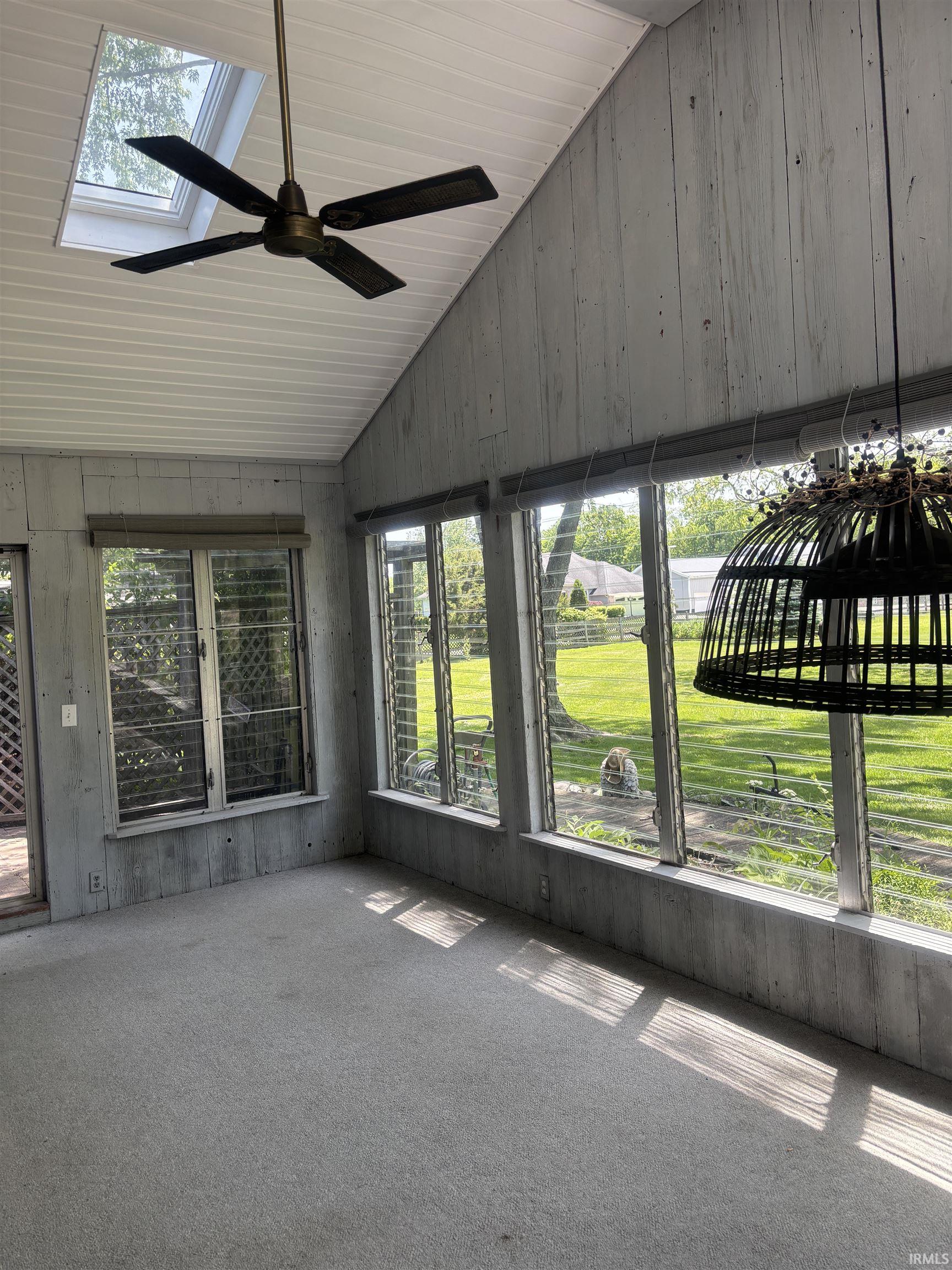 Sunroom featuring a vaulted ceiling with a skylight, a ceiling fan, and carpeted flooring
