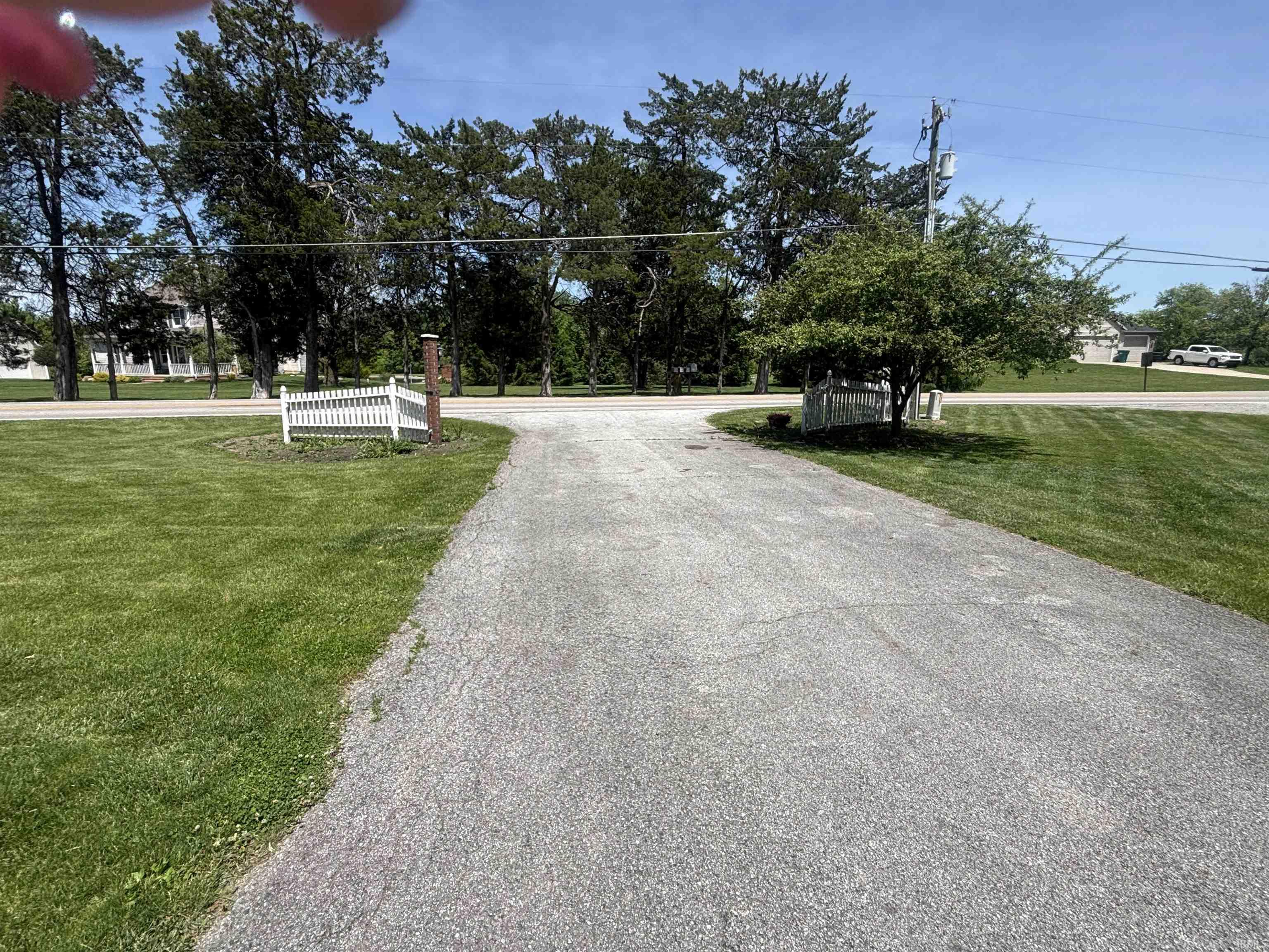 Paved driveway entrance with a decorative white picket fence and mature landscaping