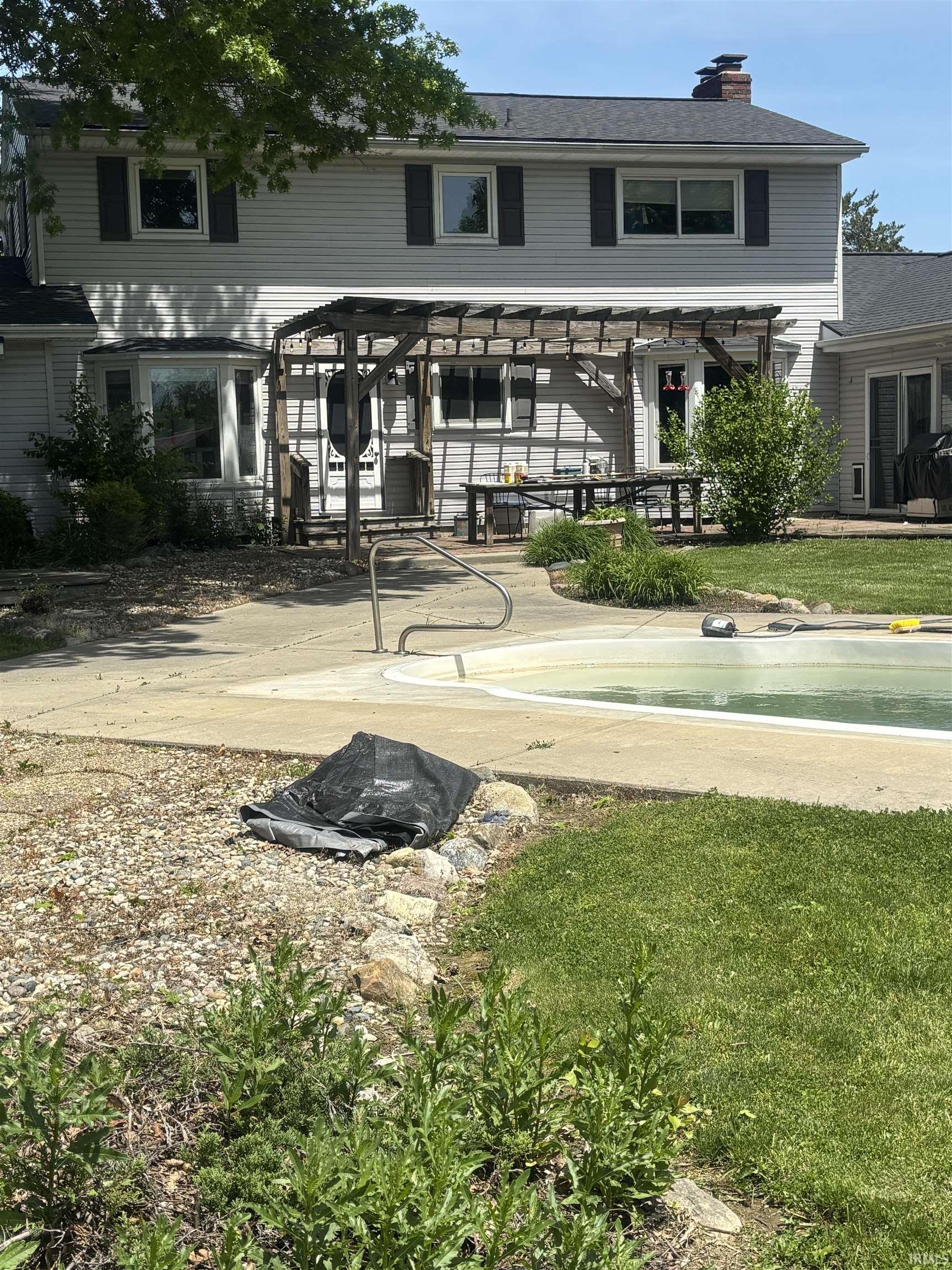 Rear exterior featuring a pergola-covered patio, bay window, and an in-ground pool with surrounding concrete decking