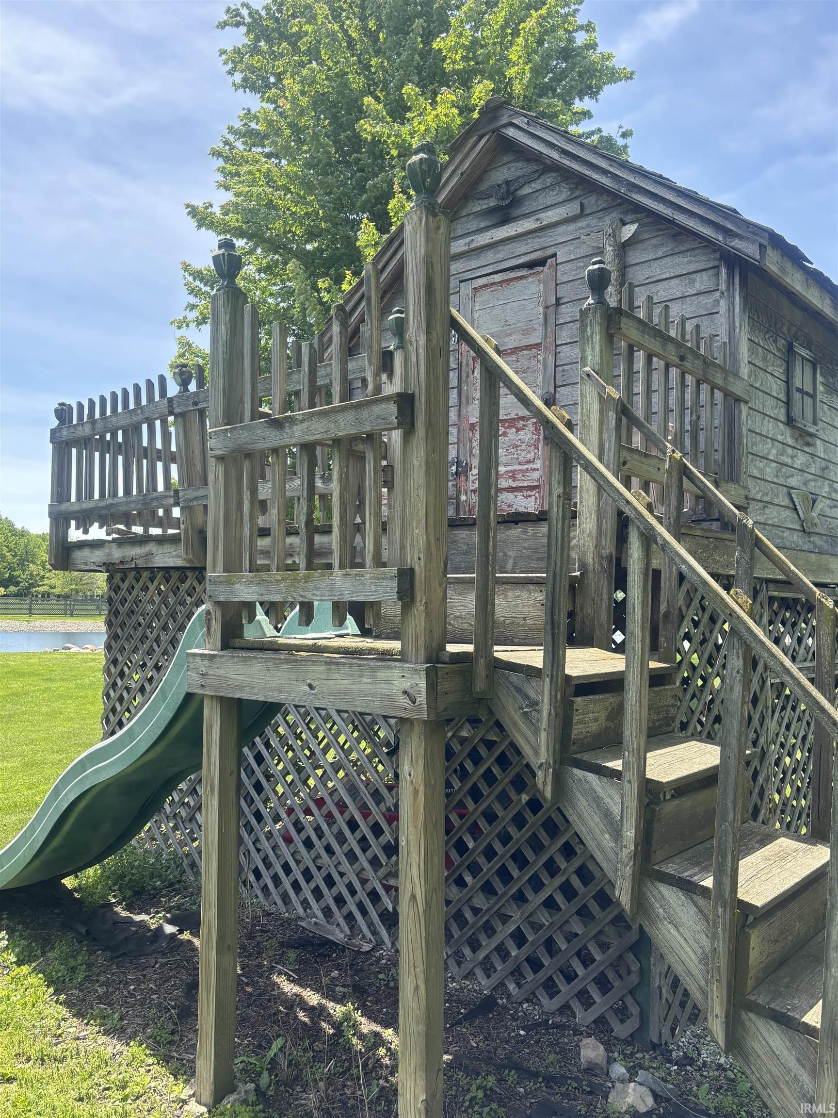 Wood-sided play structure featuring a pitched roof, an attached slide, and a staircase with a railing