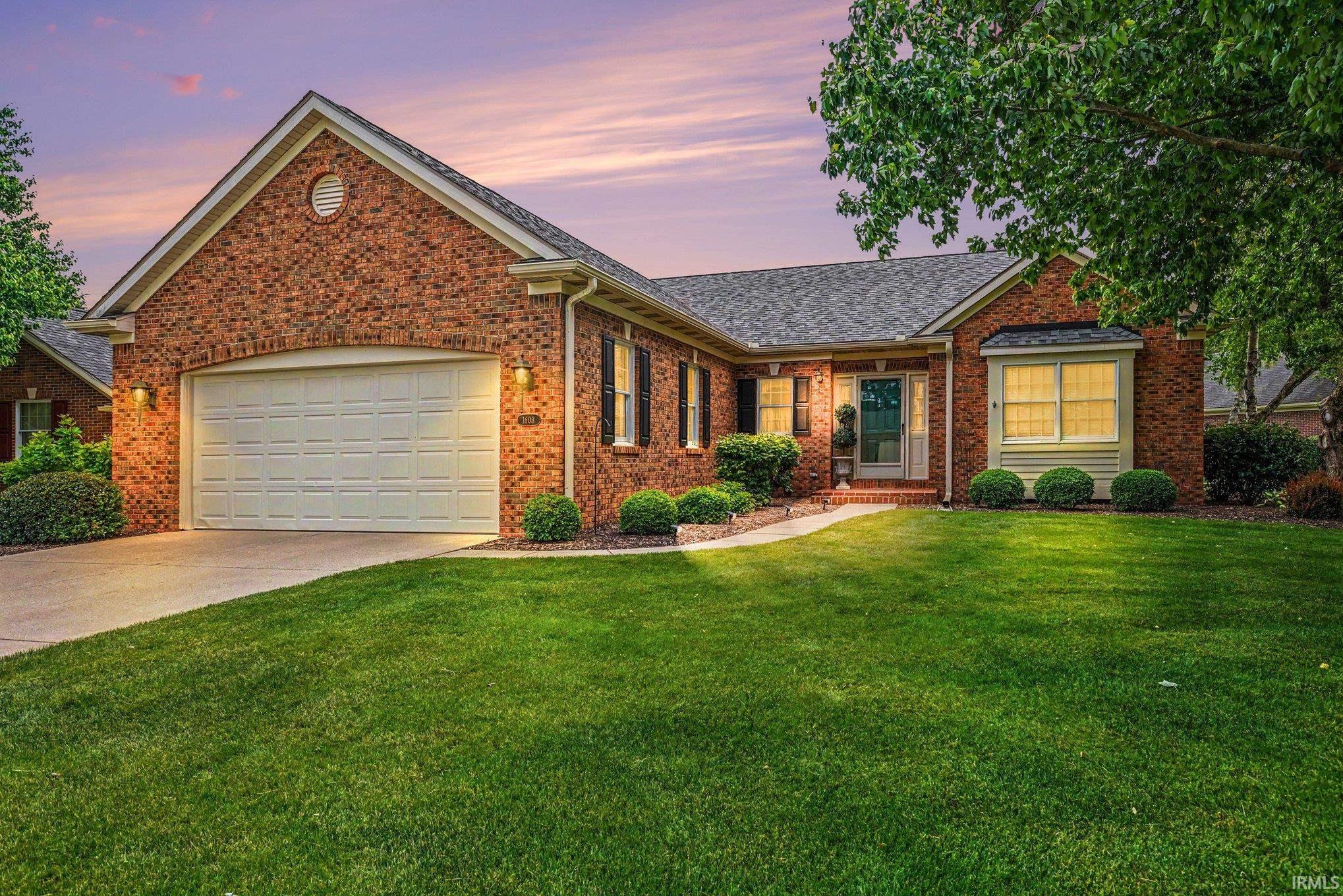 Brick facade residence featuring a two-car garage, mature landscaping, a bay window, and a concrete driveway