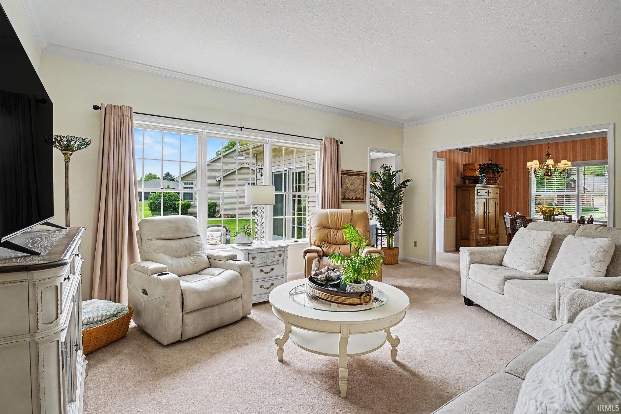 Carpeted living area featuring a large picture window, crown molding, and an open doorway to a separate dining room