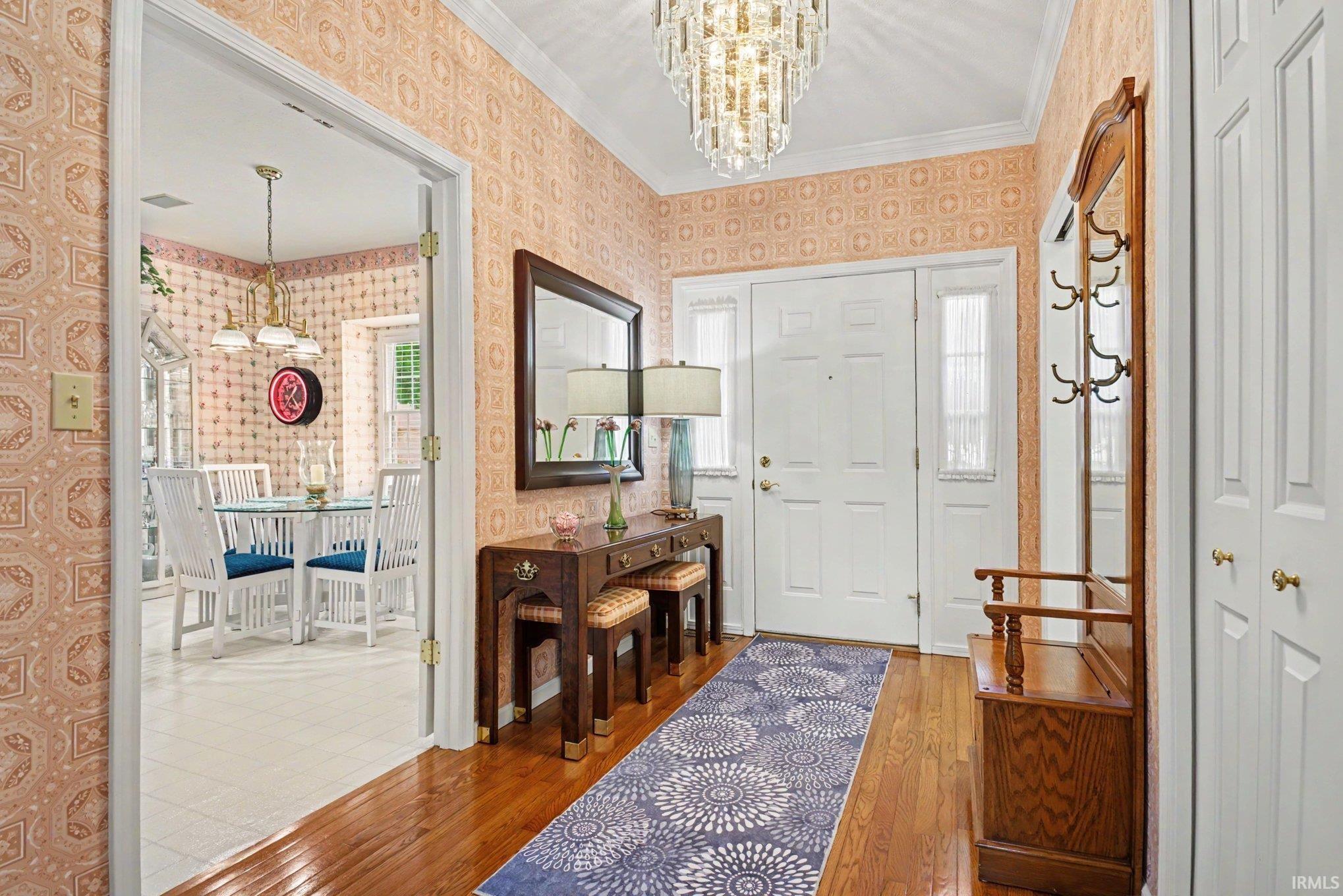Entryway featuring wood-finish flooring, a white front door with sidelights, and a crystal chandelier