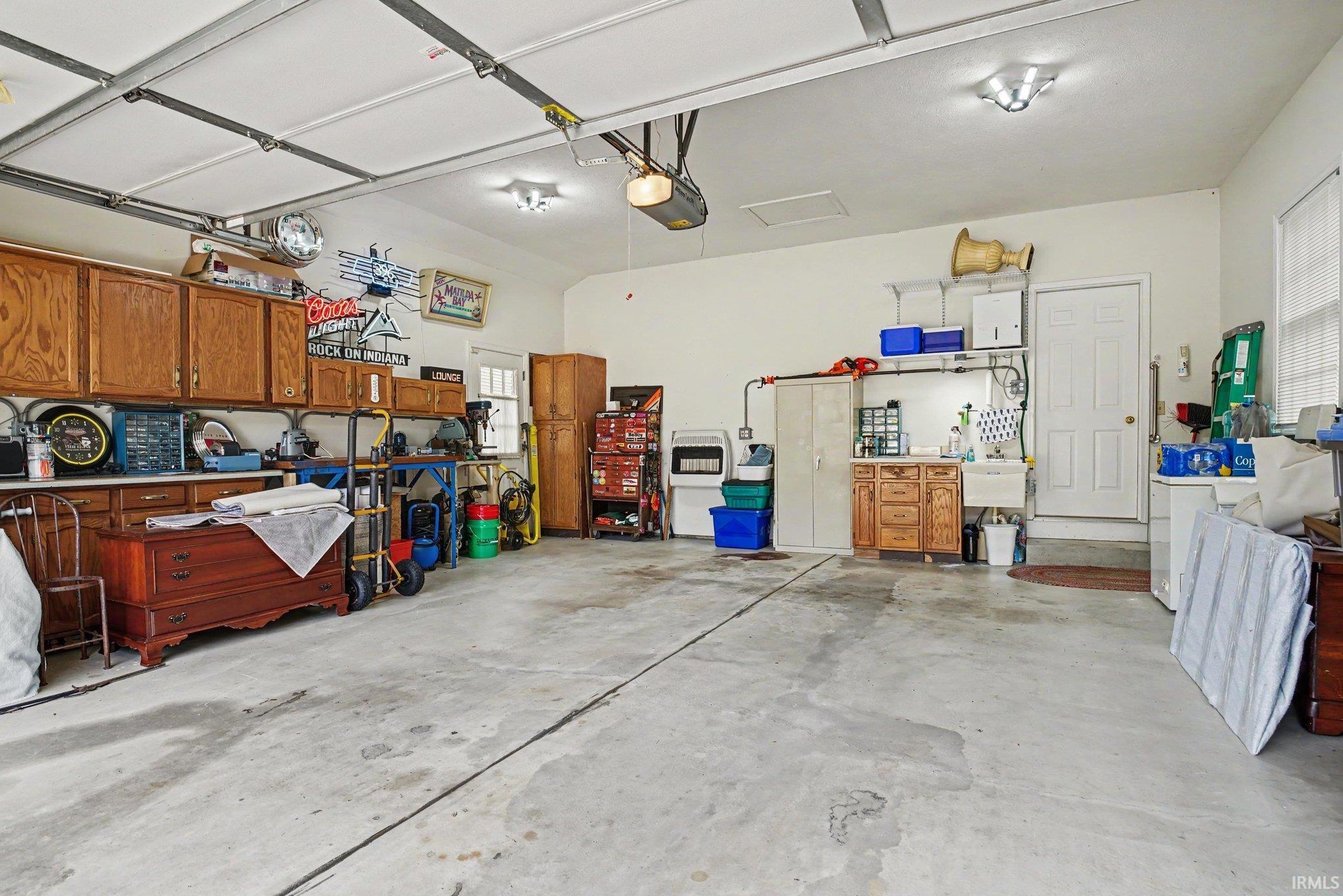Spacious garage featuring extensive built-in wooden cabinetry, a utility sink, bright overhead lighting, a garage door opener system, and a side entry door