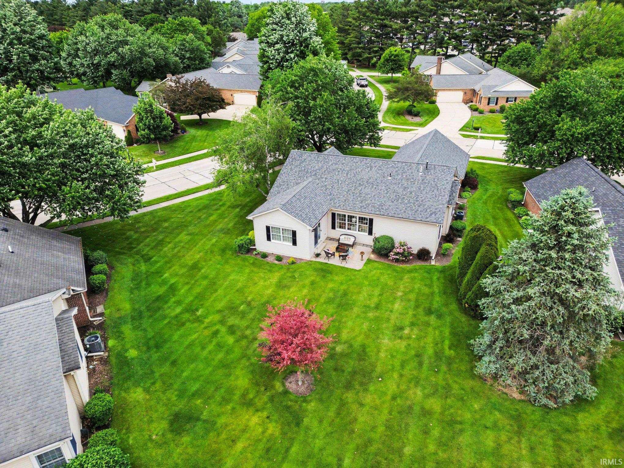 Expansive green lawn surrounds a single-story residence with a patio, mature trees, and established shrubbery