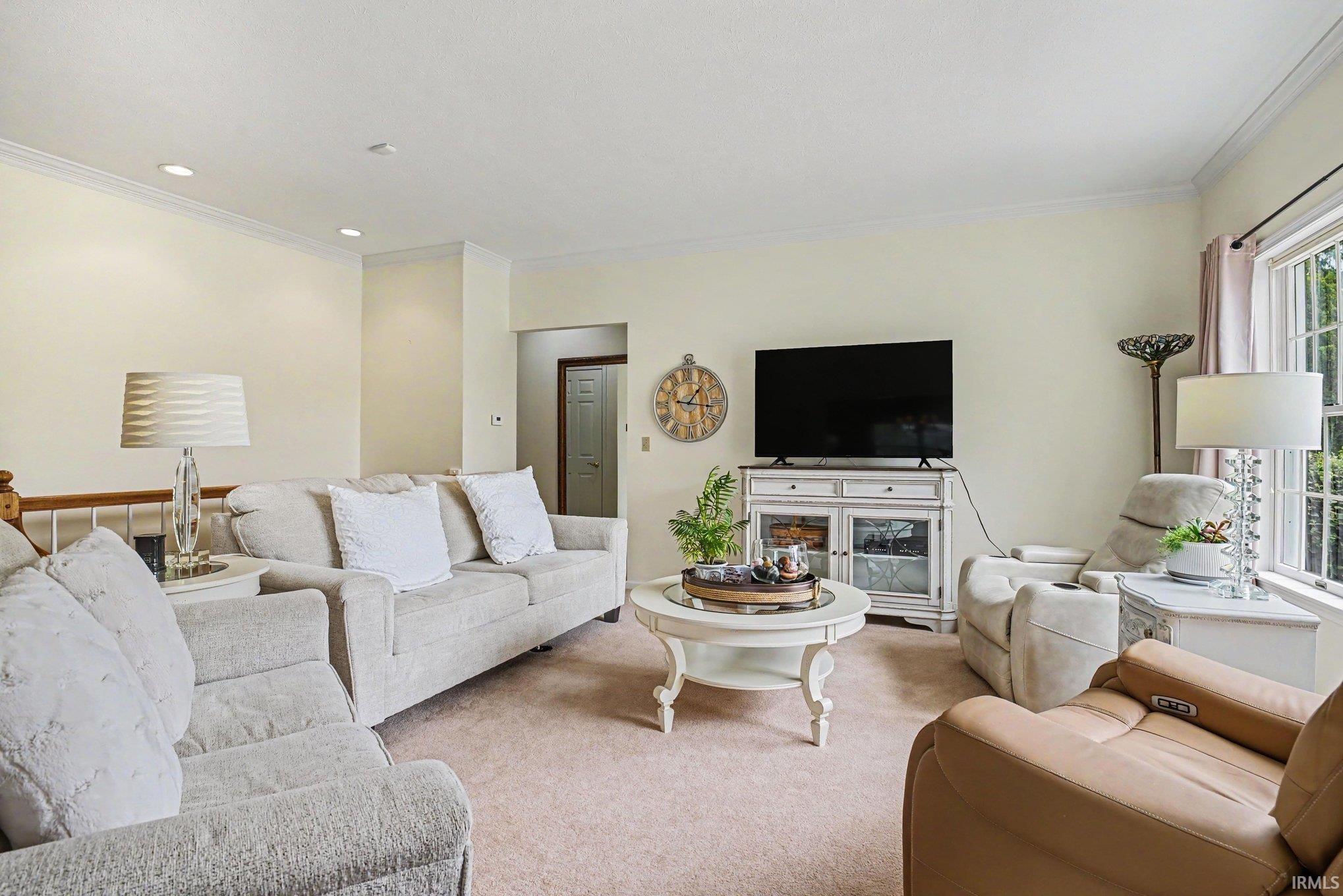 Carpeted living area featuring recessed lighting, crown molding, and a white wood-finish media console