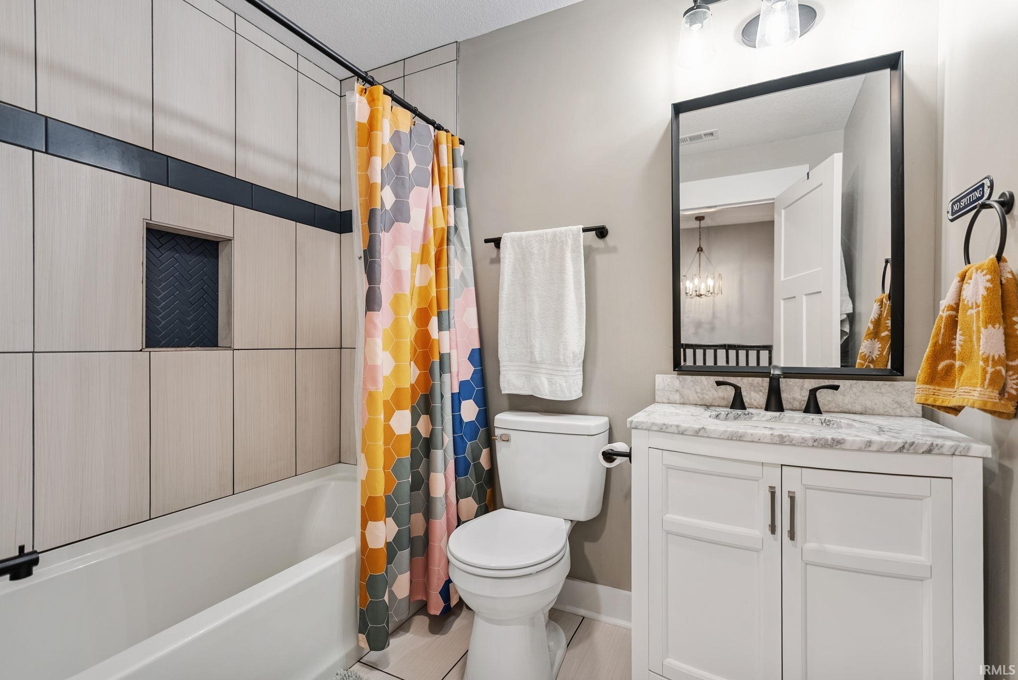 Bathroom featuring a white vanity with a light-colored countertop, a rectangular black-framed mirror, a black wall-mounted faucet, and a tub with light-toned vertical tiling