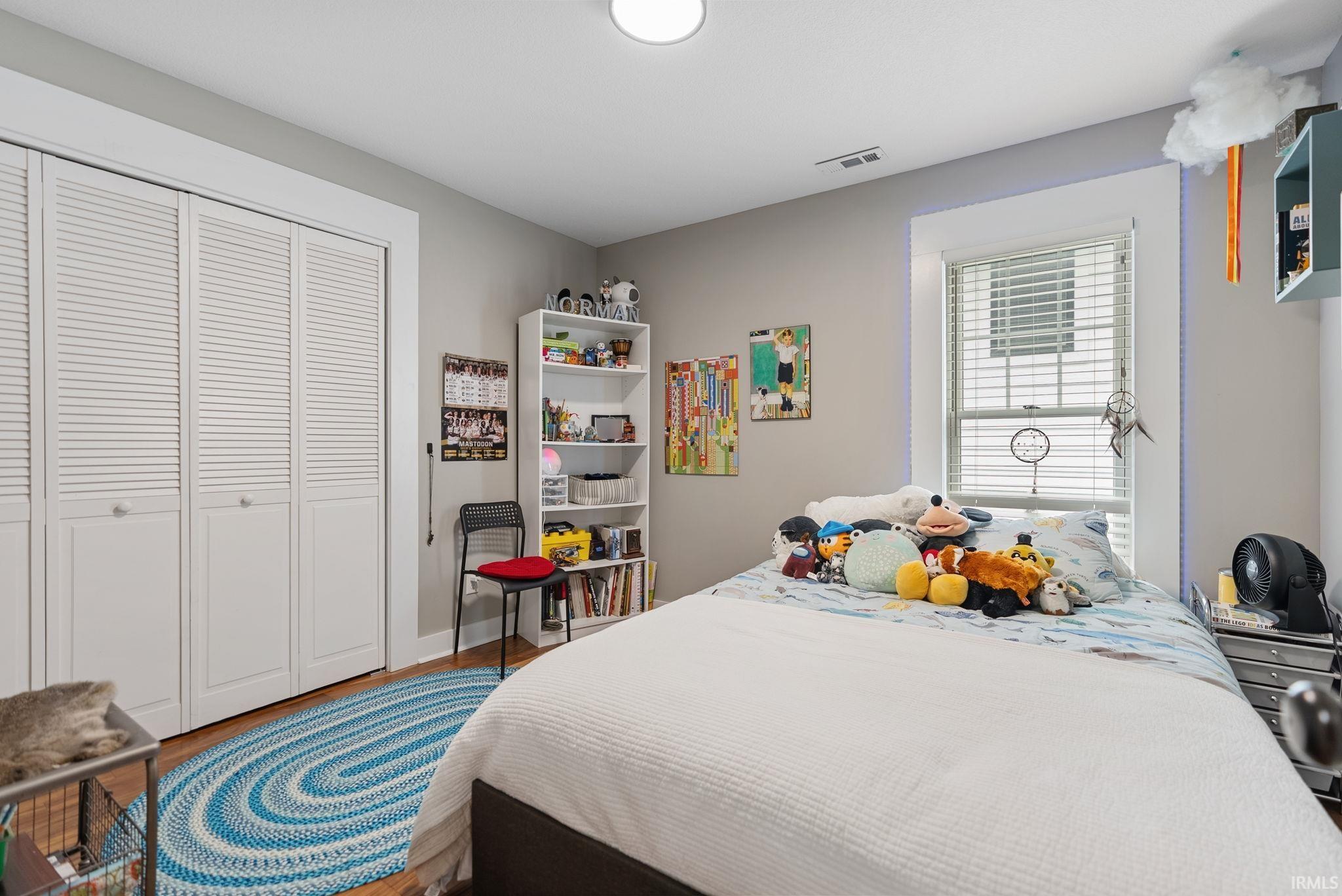 Bedroom featuring wood-finish flooring, a double window with blinds, and white louvered bifold closet doors
