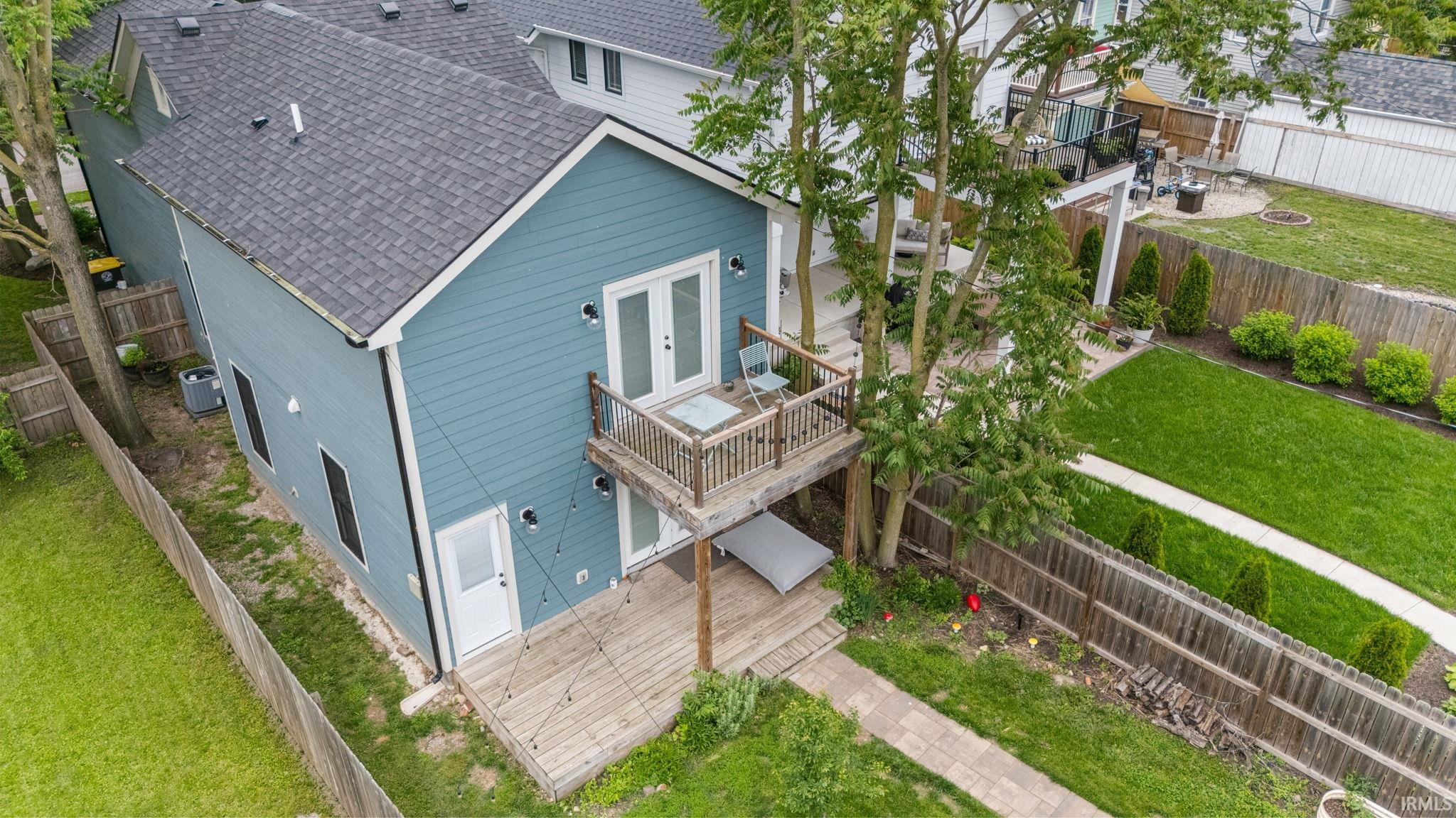 Rear exterior showcasing a second-story balcony with French doors, a ground-level deck, a fenced yard, and an established lawn with a paver pathway