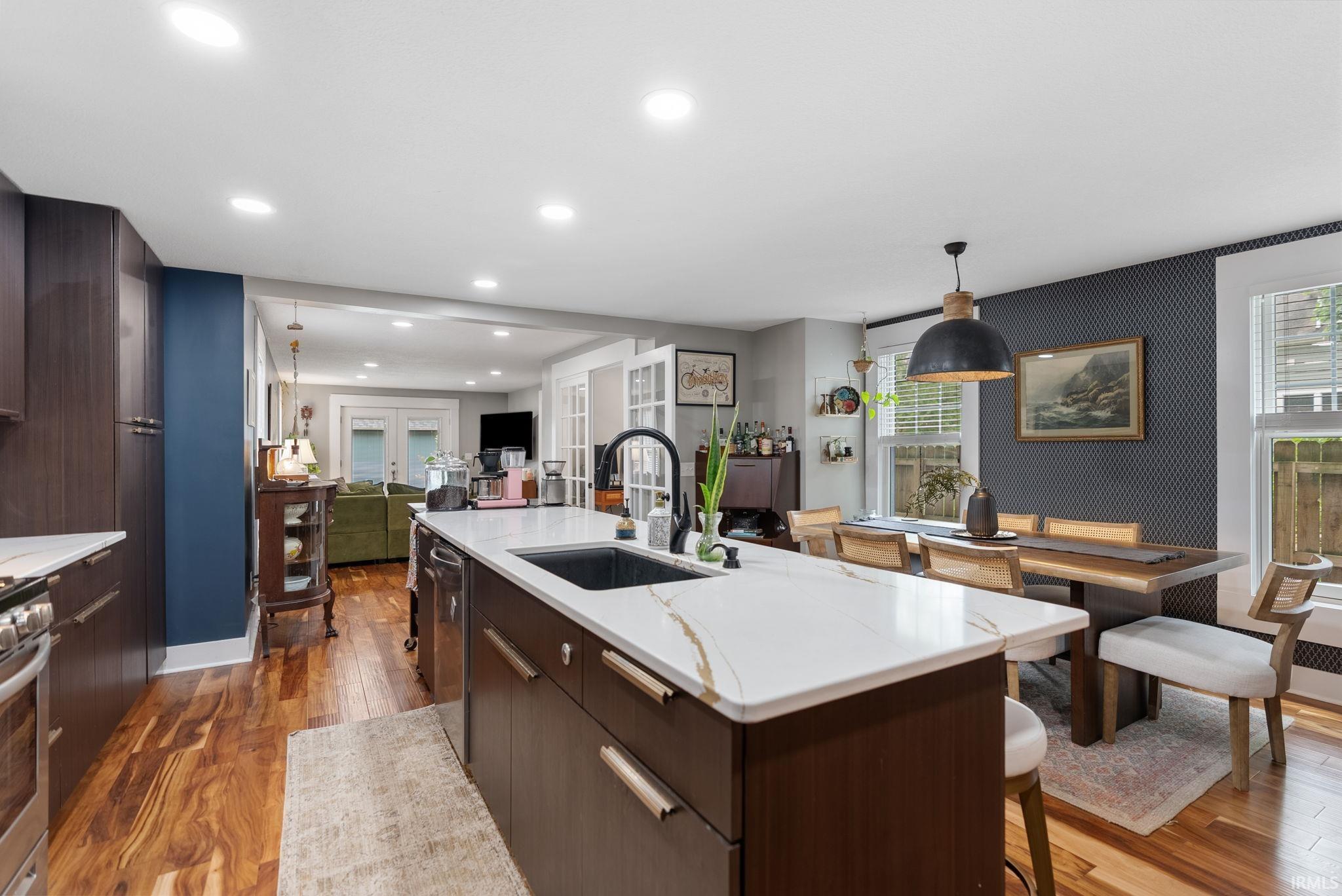 Open-concept kitchen featuring a spacious island with a built-in sink, white stone-finish countertop, and rich wood-finish cabinetry
