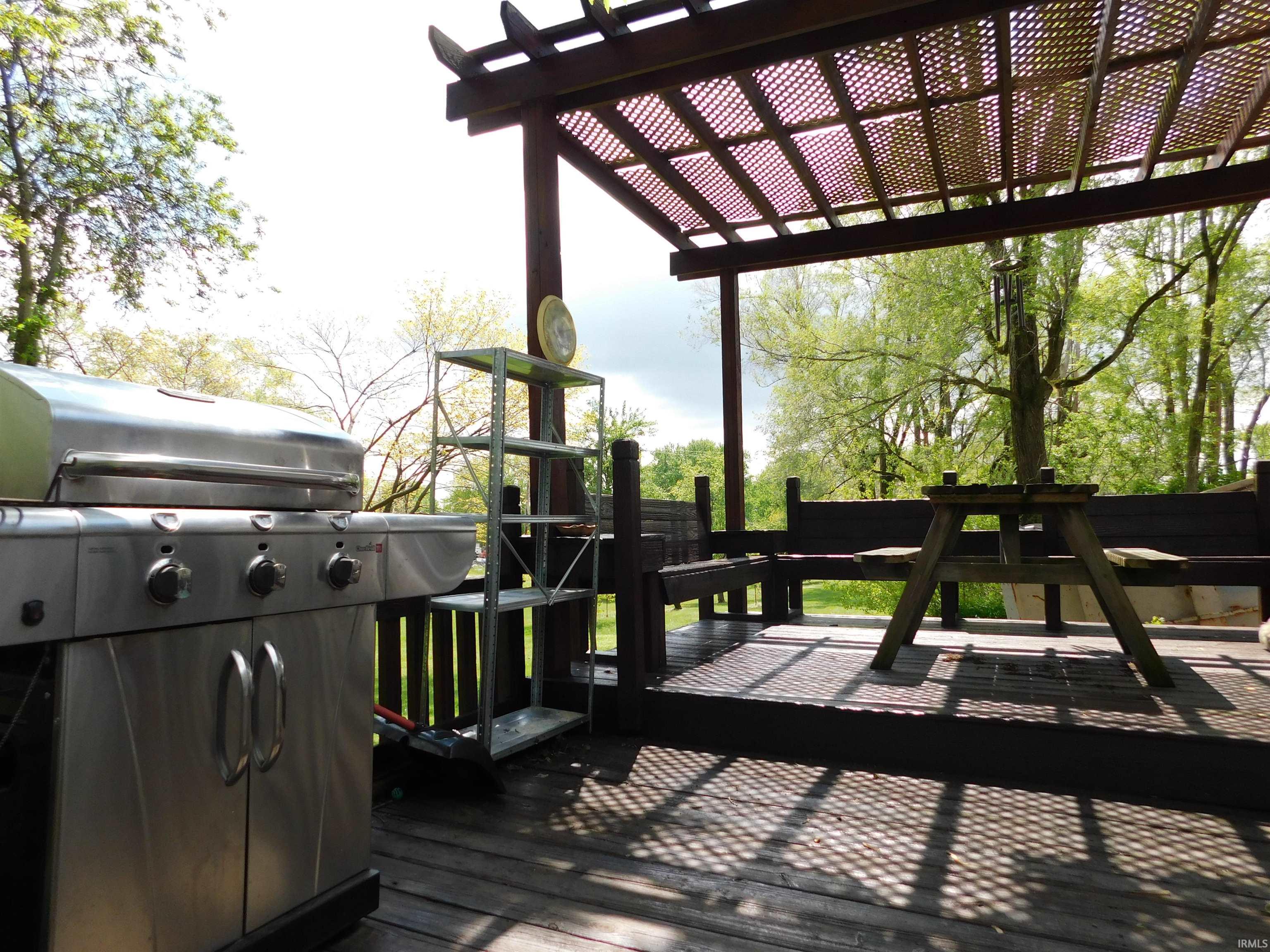 Expansive outdoor deck featuring a patterned pergola overhead, built-in wooden bench seating, and natural tree scenery