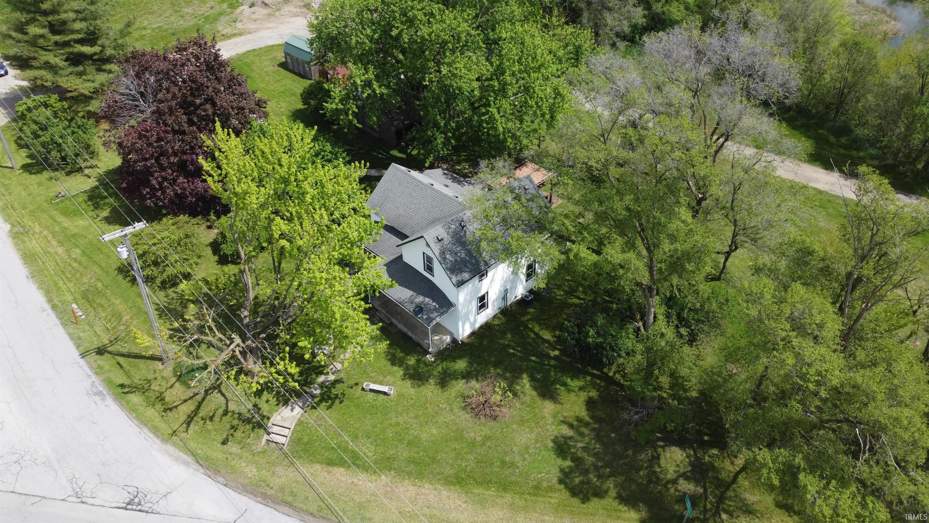 White siding residence with a dark shingled roof, surrounded by mature trees and verdant landscaping