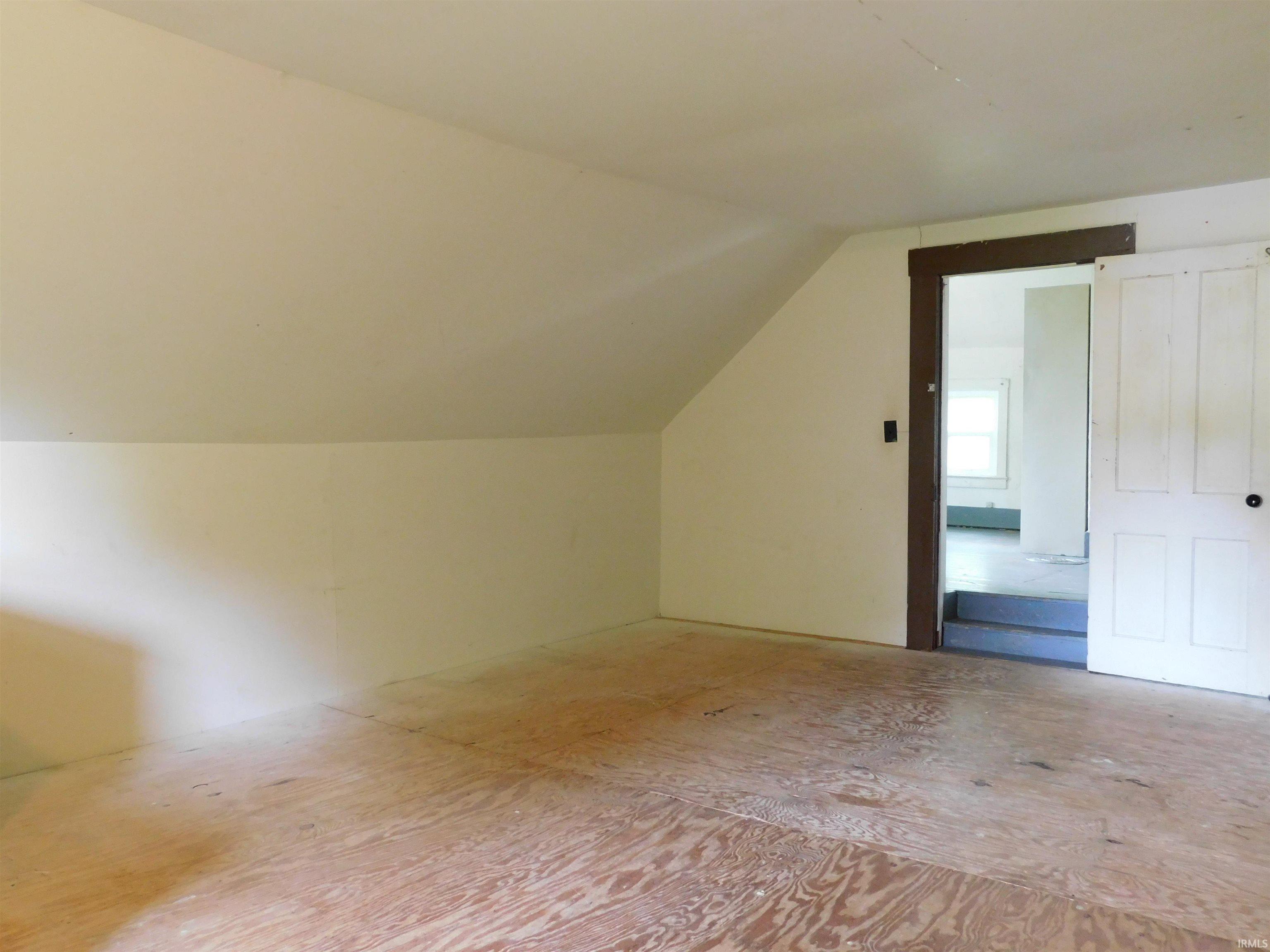 Spacious attic room featuring plywood flooring and sloped ceilings