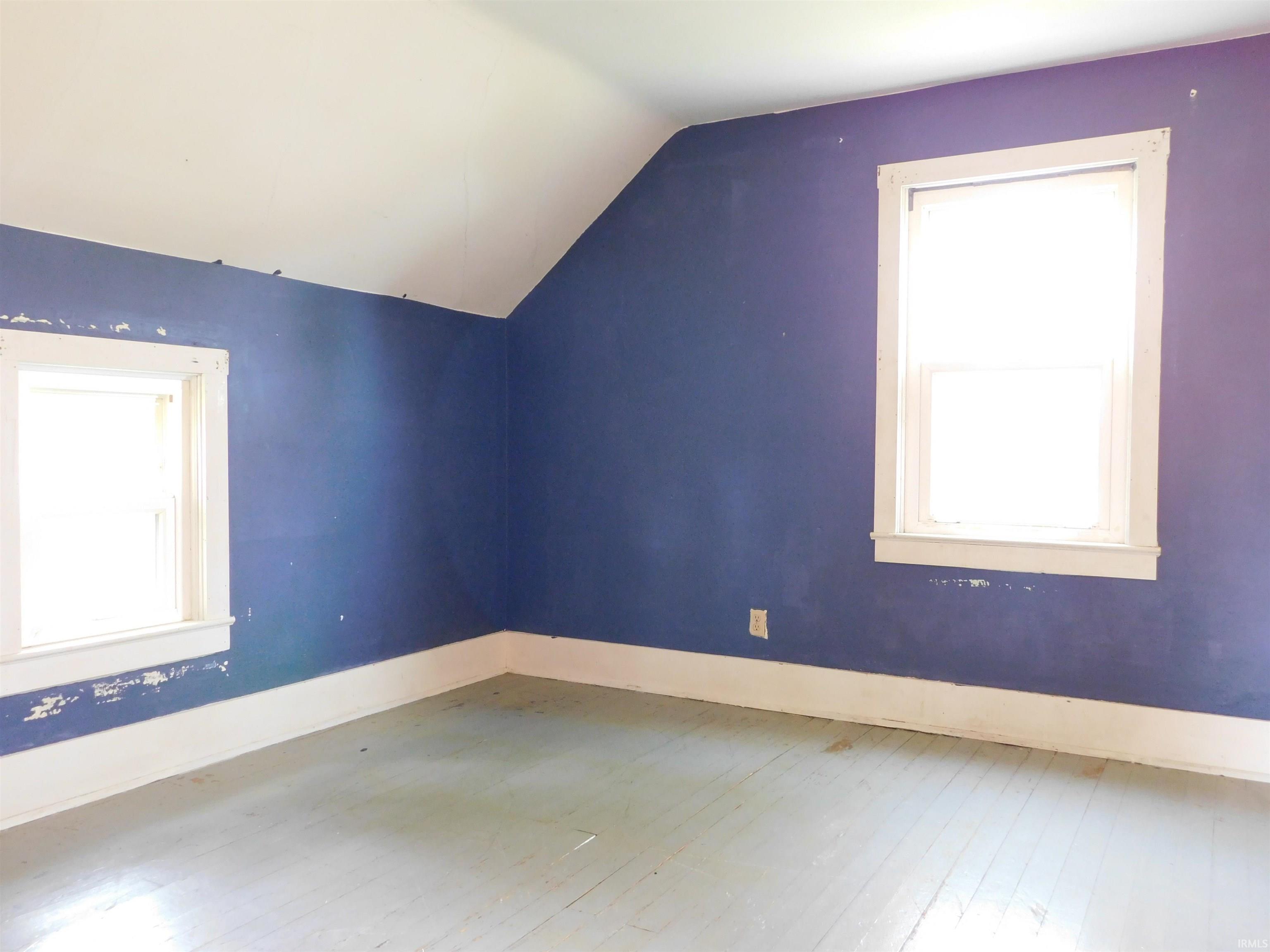 Room featuring two windows, painted wood-finish flooring, white baseboards, and a sloped ceiling