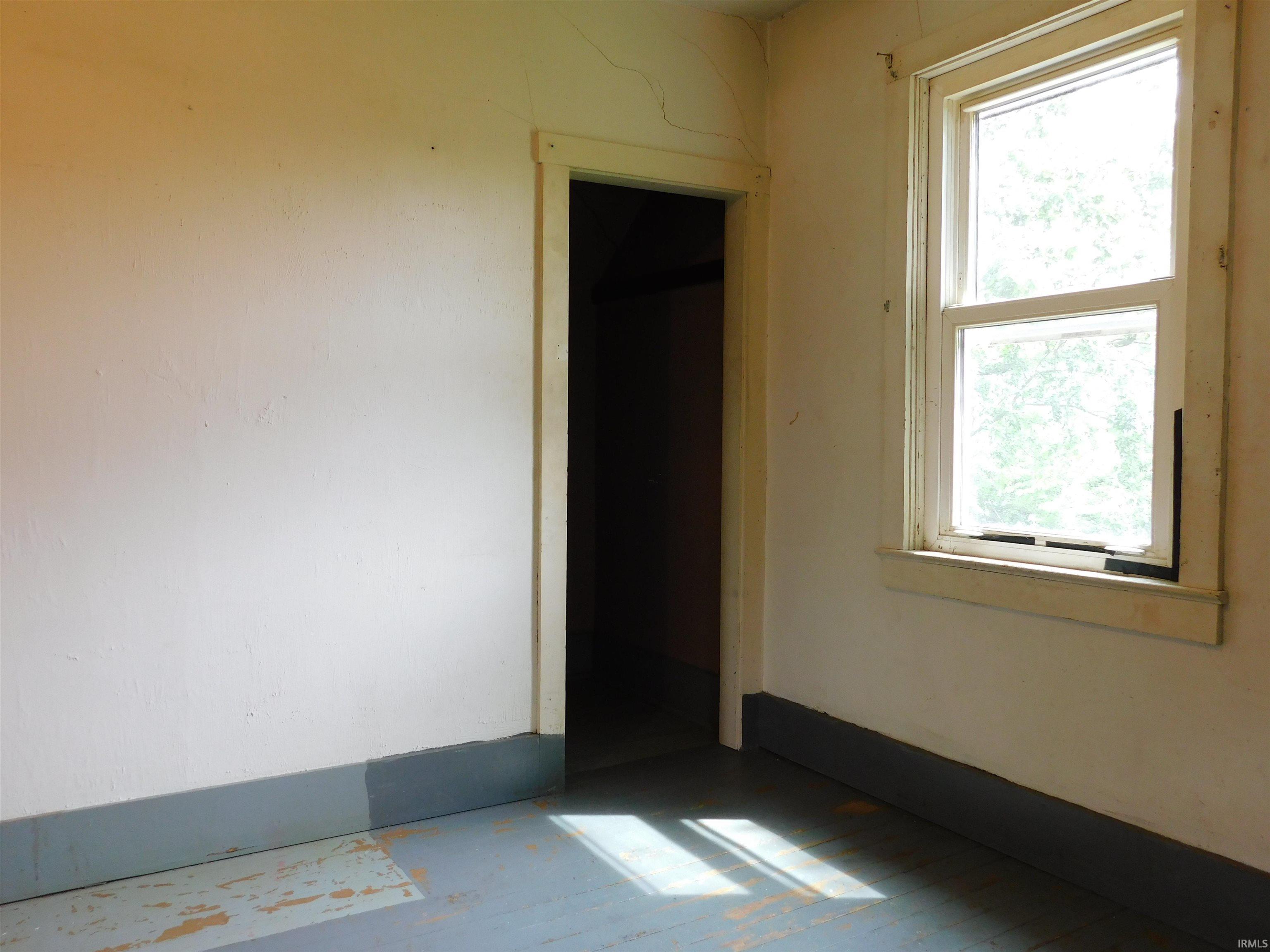 Room featuring a double-hung window with wood trim, a doorway, painted walls, and painted wood flooring