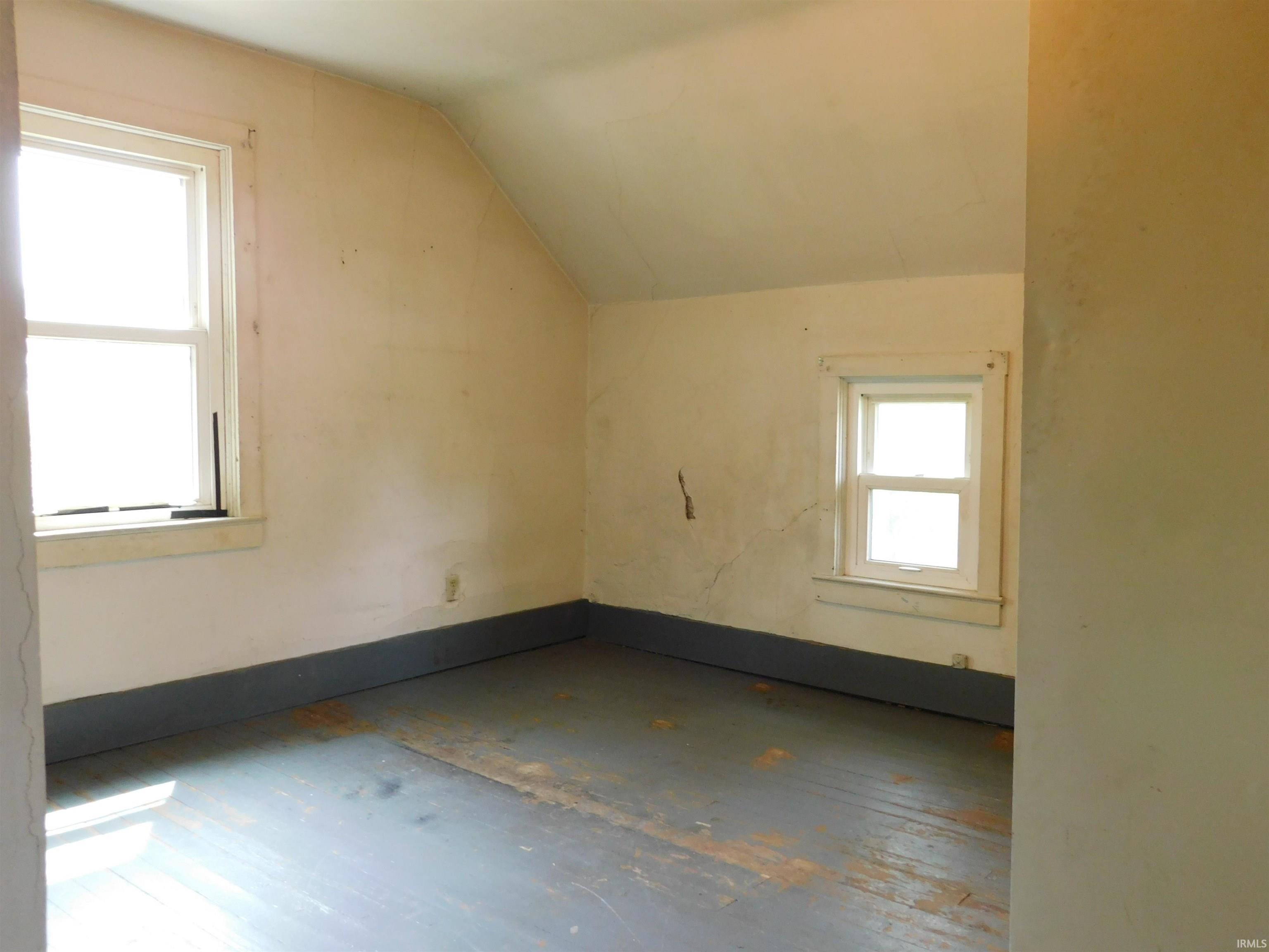 Room featuring painted wood-finish flooring, two distinct window frames, and an angled ceiling