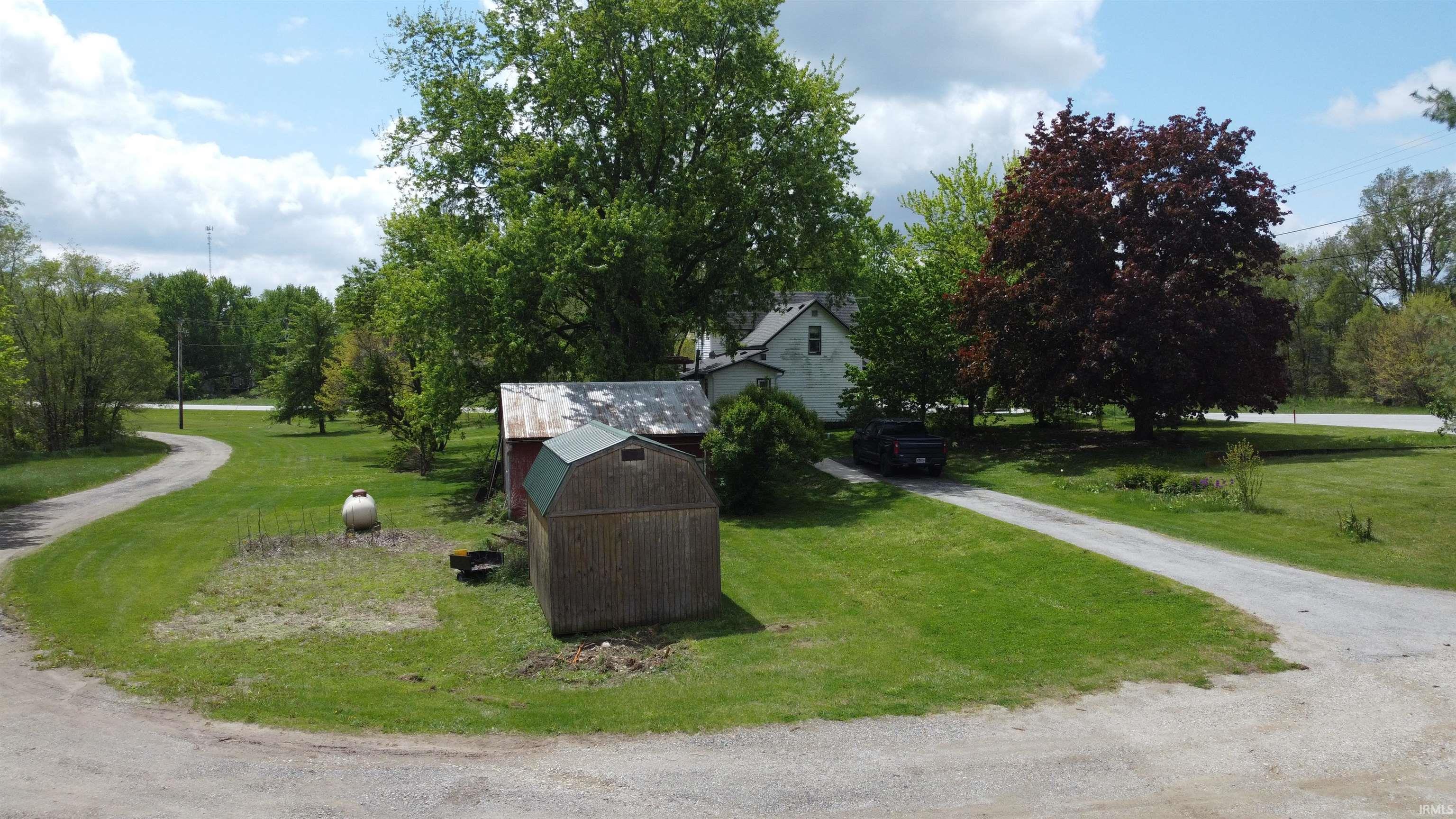 Expansive property featuring a white residence, a detached red utility shed, and a wooden storage shed with a green gambrel roof