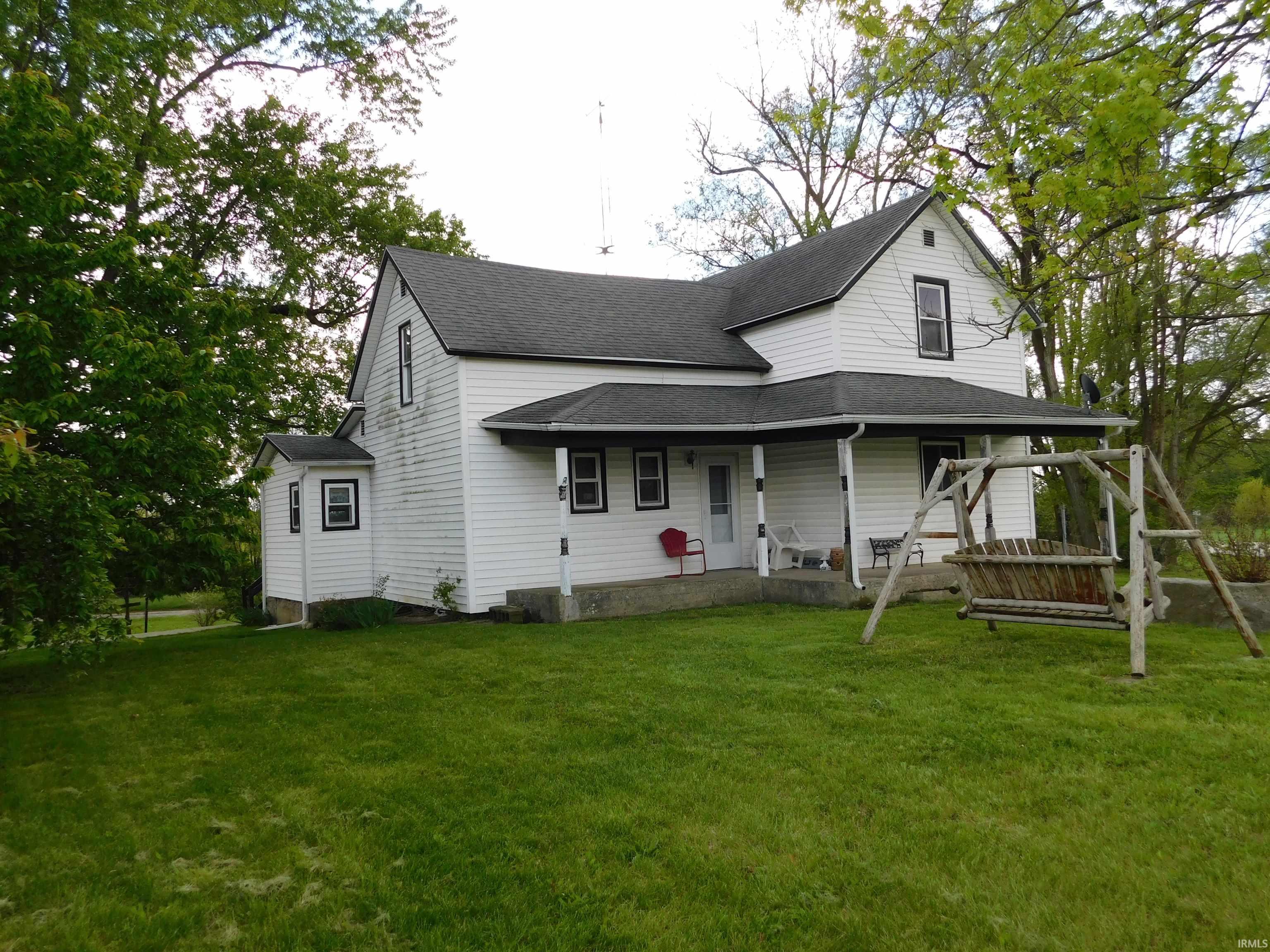 White siding exterior with a dark shingle roof, featuring a covered porch and mature trees