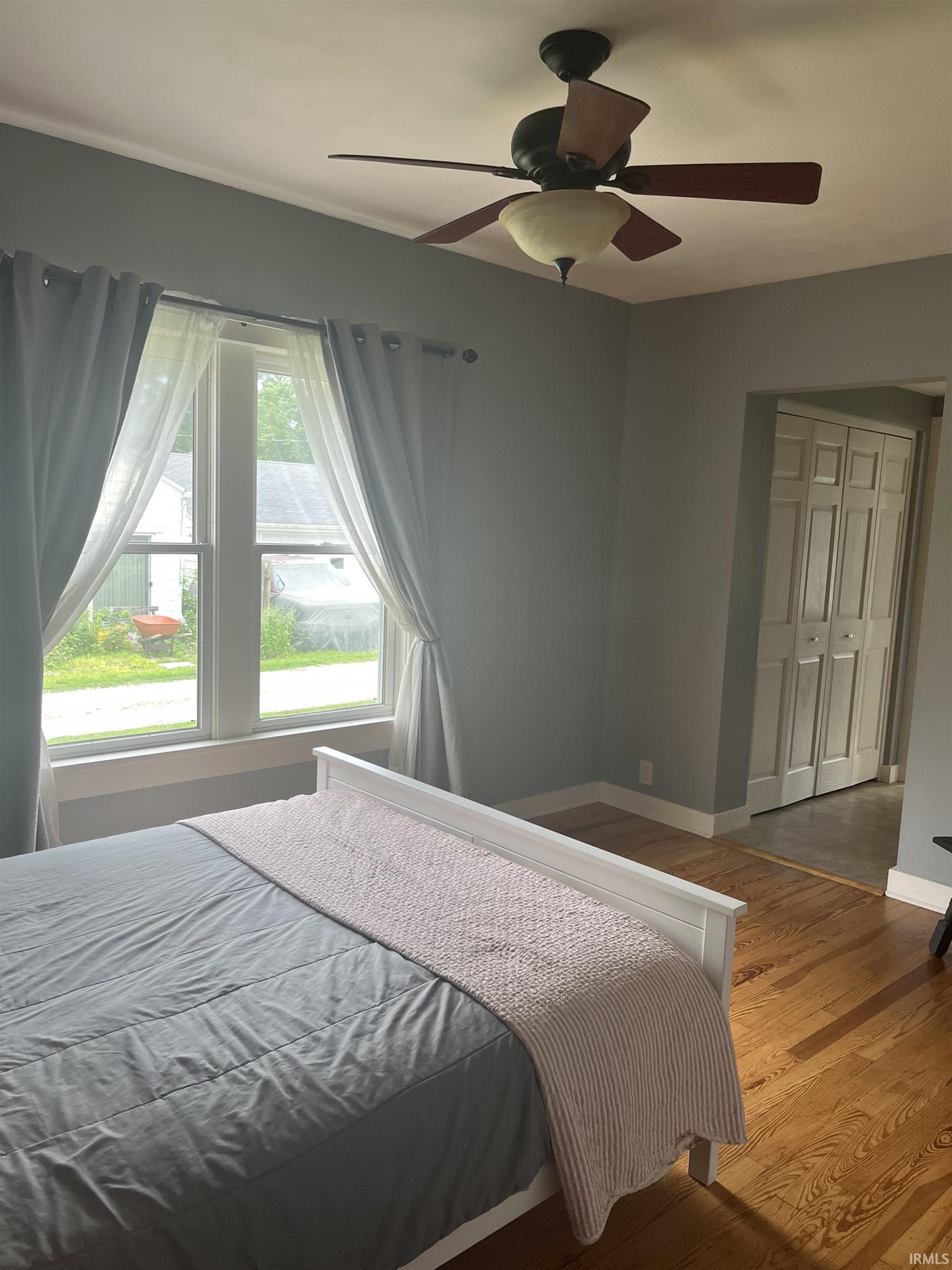 Room featuring wood-finish flooring, a ceiling fan with integrated lighting, and a window with white trim