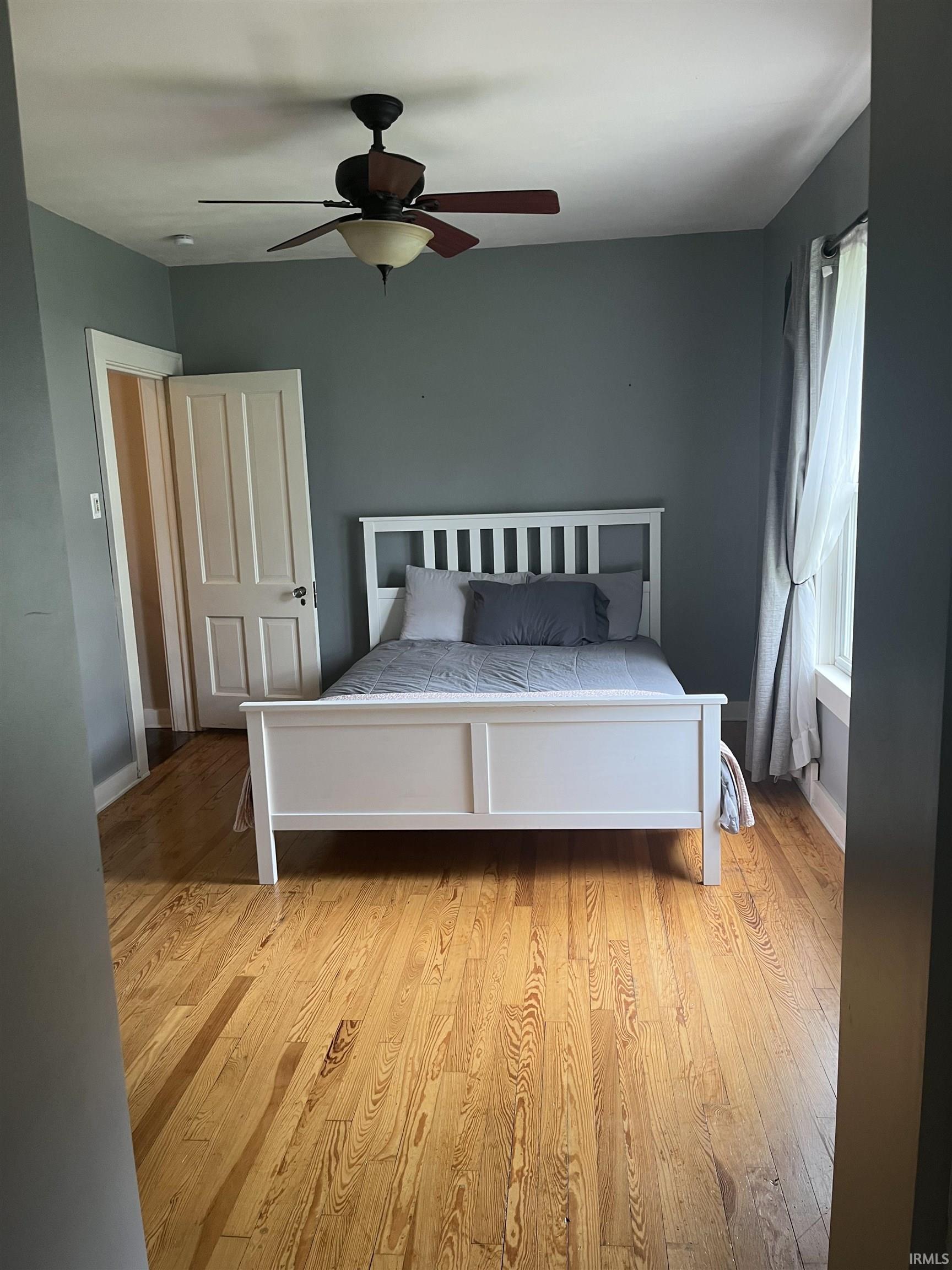Bright room featuring wood-finish flooring, a ceiling fan with integrated lighting, and a white paneled door