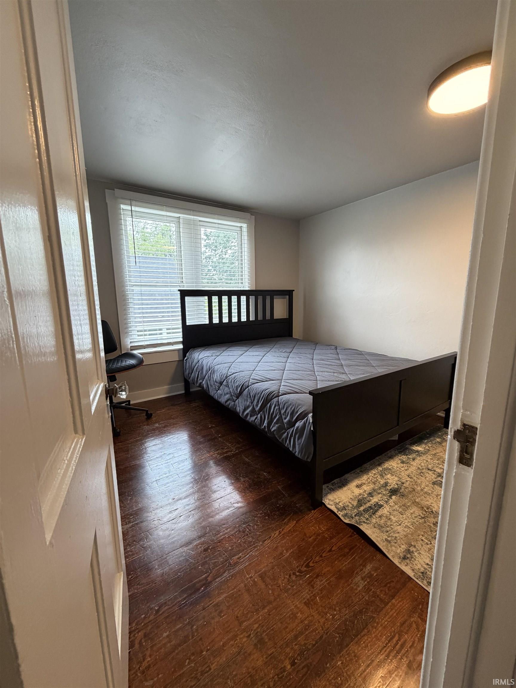 Interior room featuring wood-finish flooring, a window with horizontal blinds, and a flush-mount ceiling light fixture
