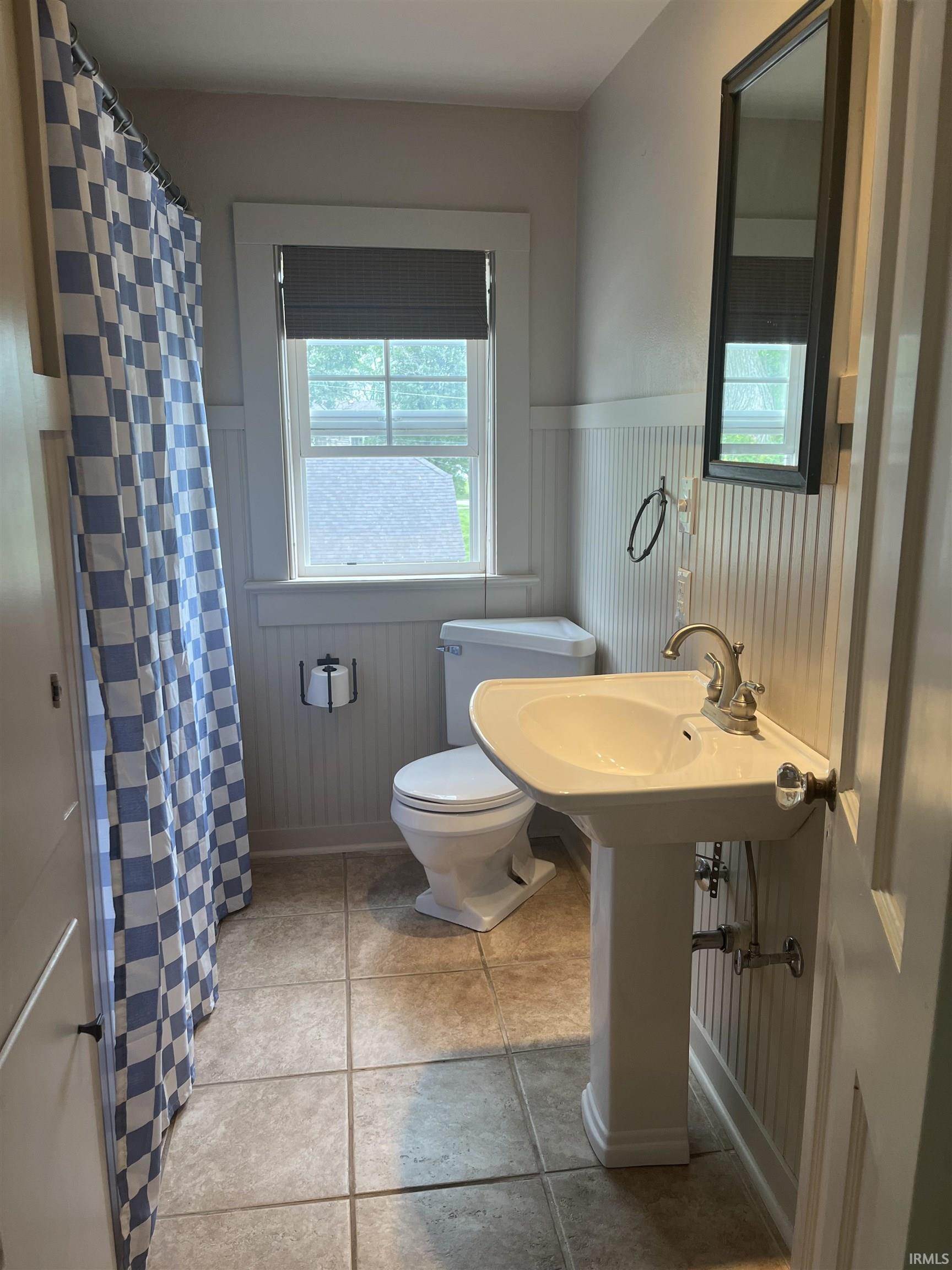 Pedestal sink featuring a chrome faucet, toilet, and a window with a dark privacy shade