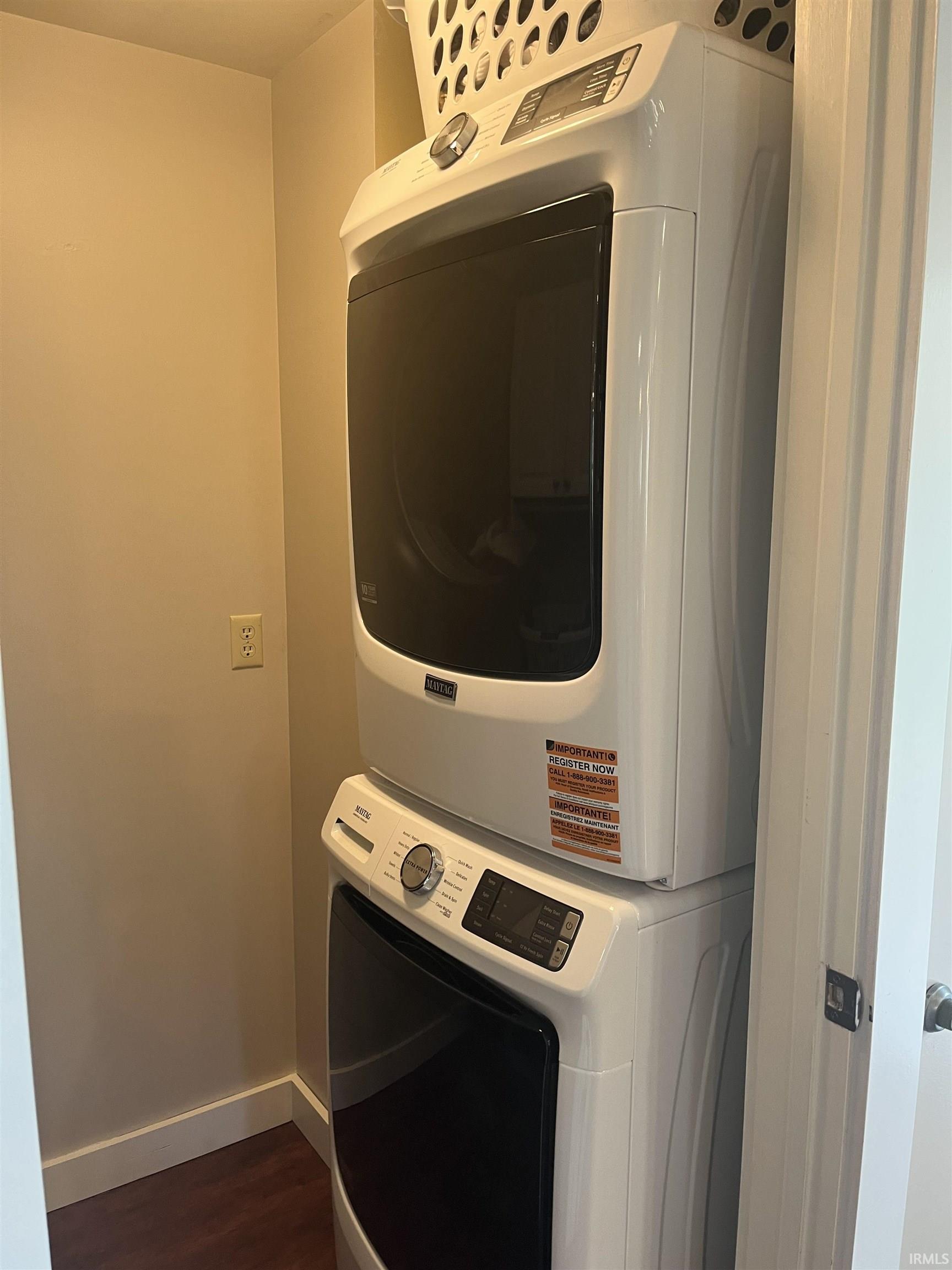 Dedicated laundry closet featuring a stacked white washer and dryer unit, wood-finish flooring, and light neutral walls
