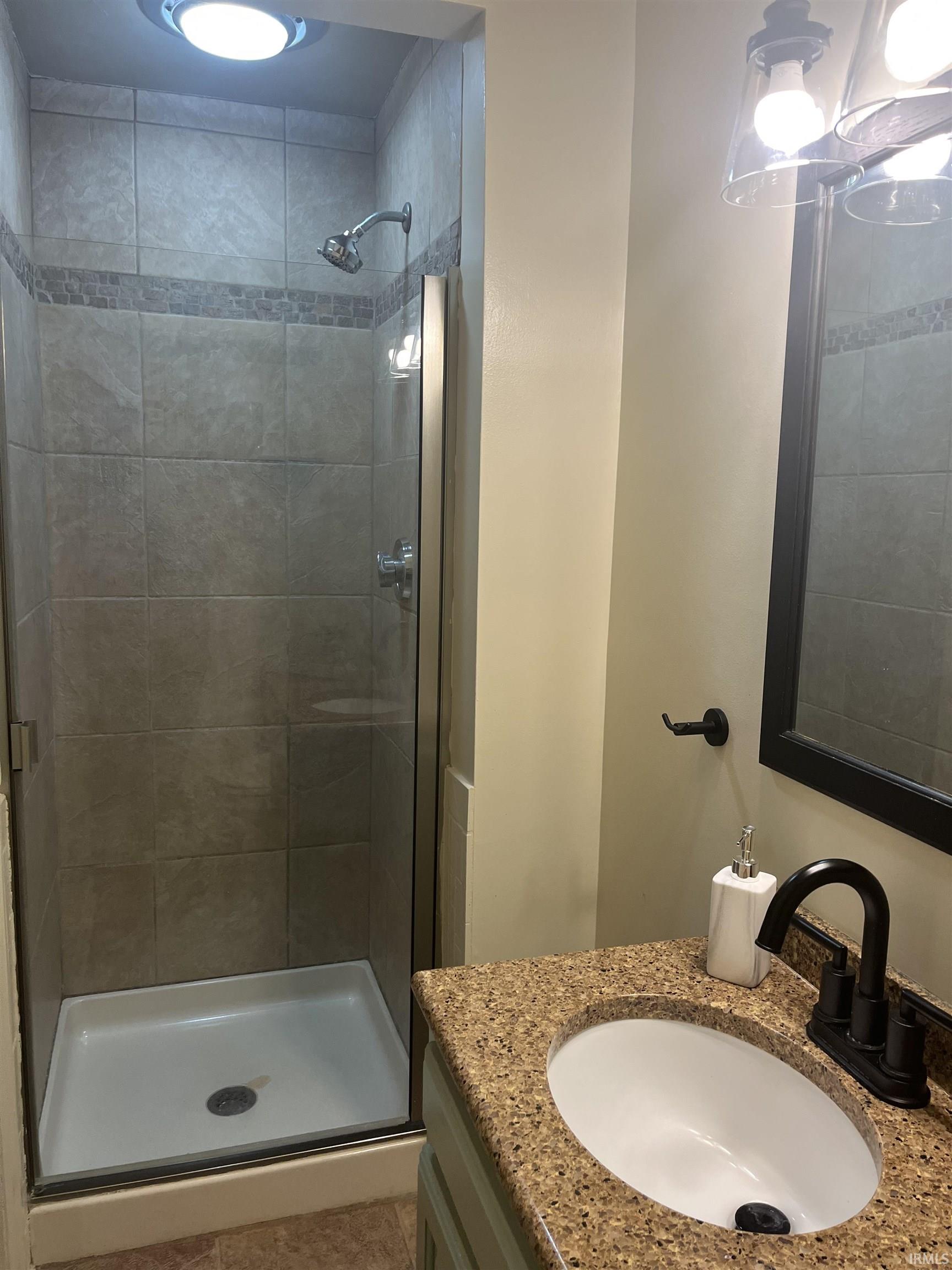 Tiled shower with glass enclosure, white base, and a mosaic accent band