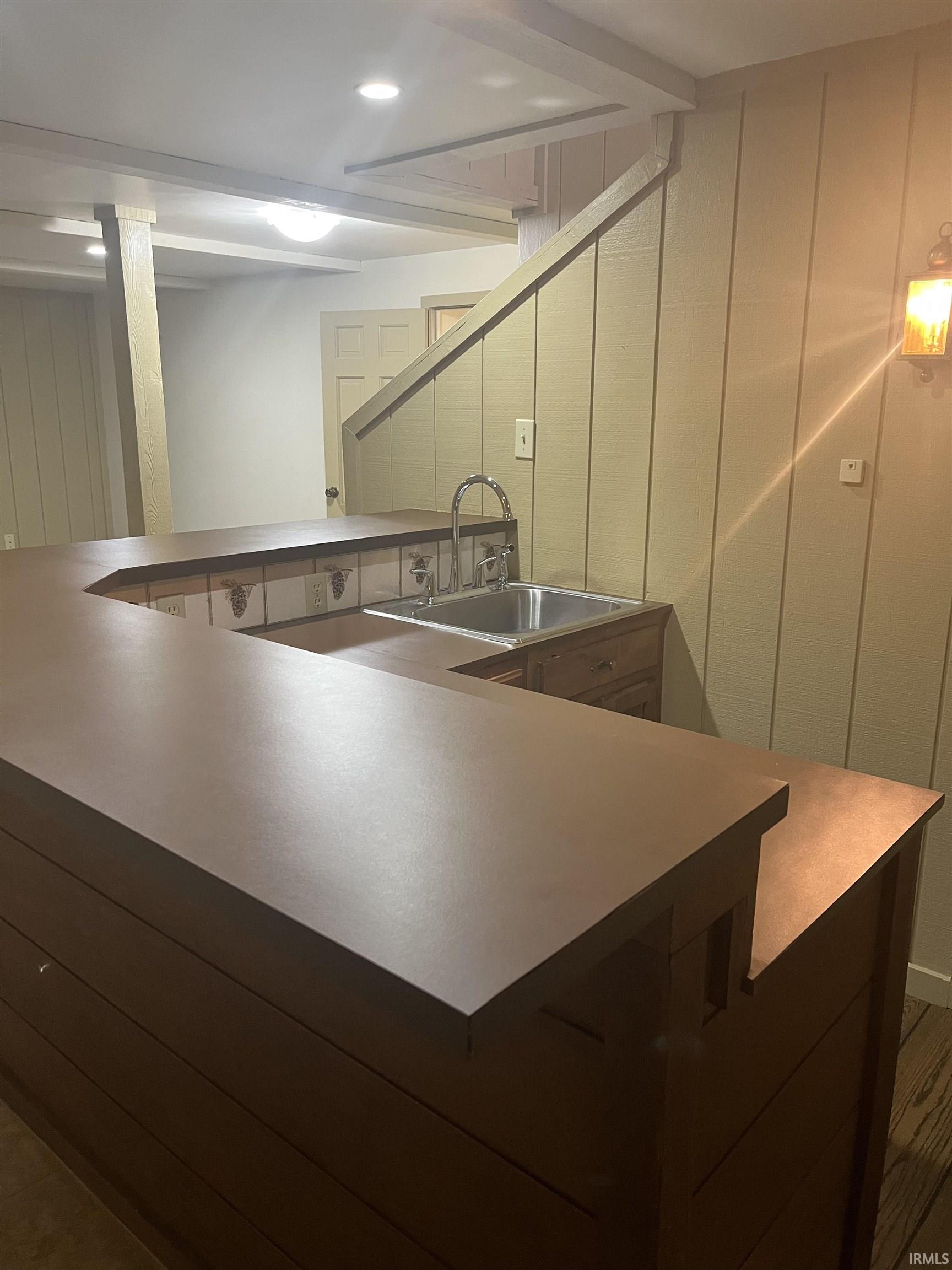 U-shaped bar featuring a stainless steel sink with gooseneck faucet, wood-finish countertops, tile backsplash, and integrated wood-panel cabinetry