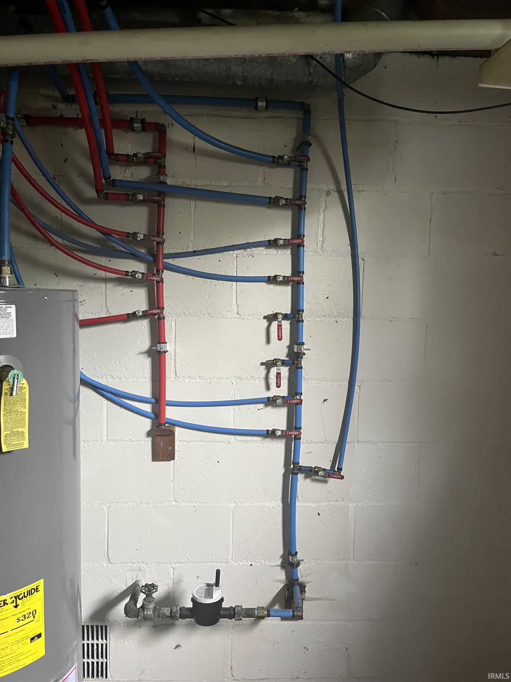 Utility area featuring a water heater, visible PEX plumbing, individual shut-off valves, a water meter, and a cinder block wall