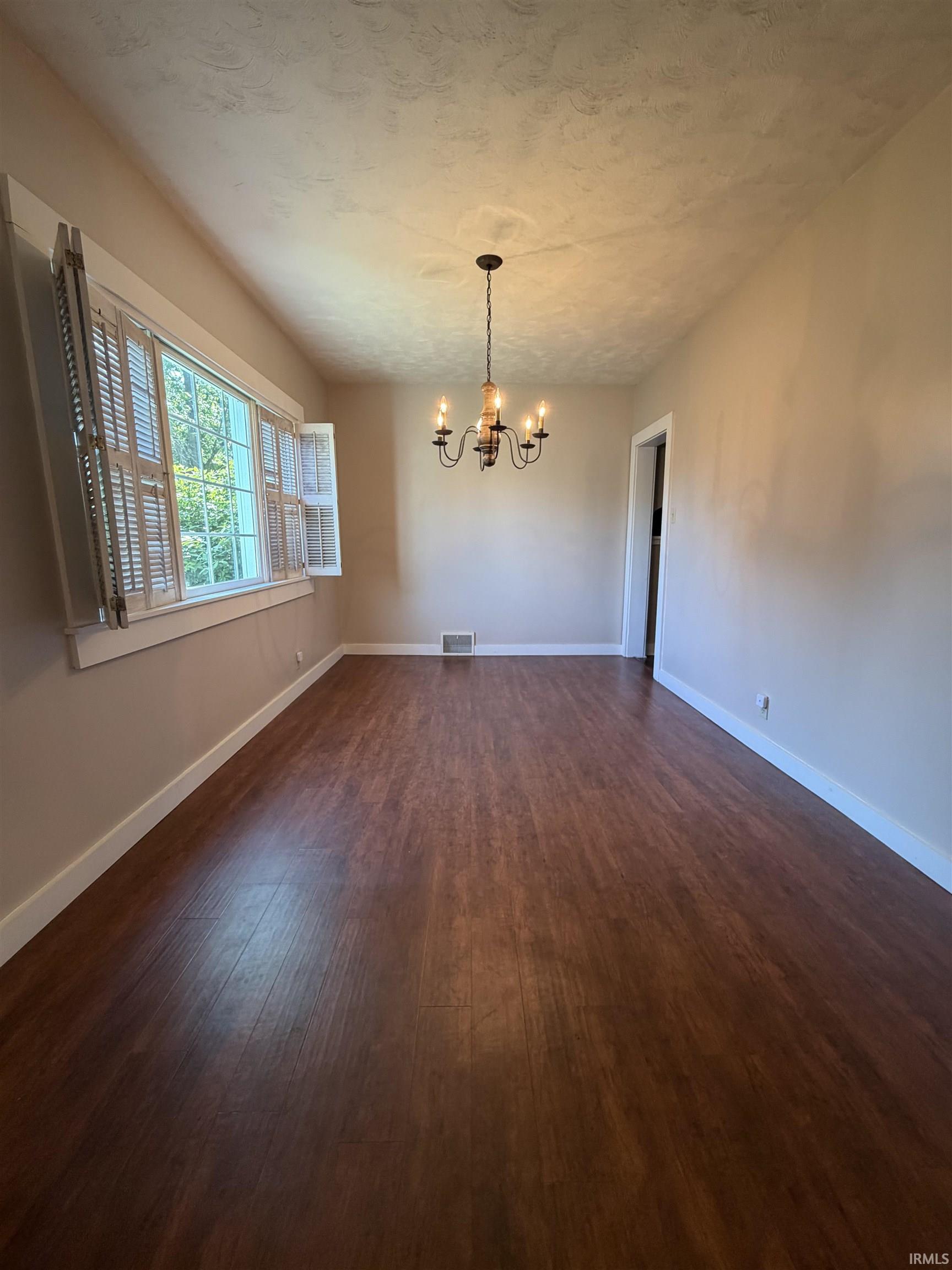 Spacious room featuring wood-finish flooring, neutral-toned walls, and a multi-arm chandelier