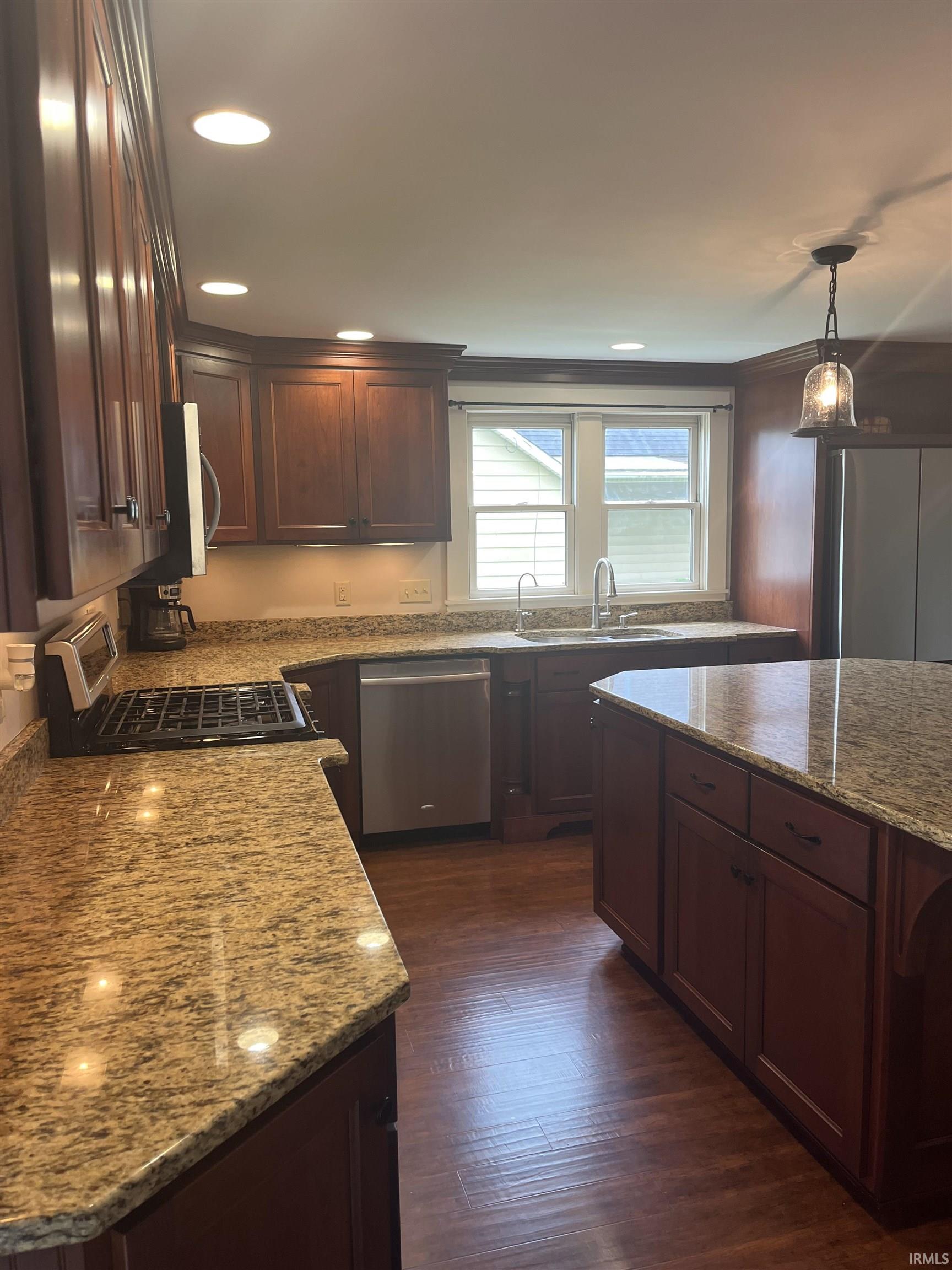 Kitchen featuring rich wood cabinetry, granite countertops, stainless steel appliances, recessed lighting, and wood-finish flooring
