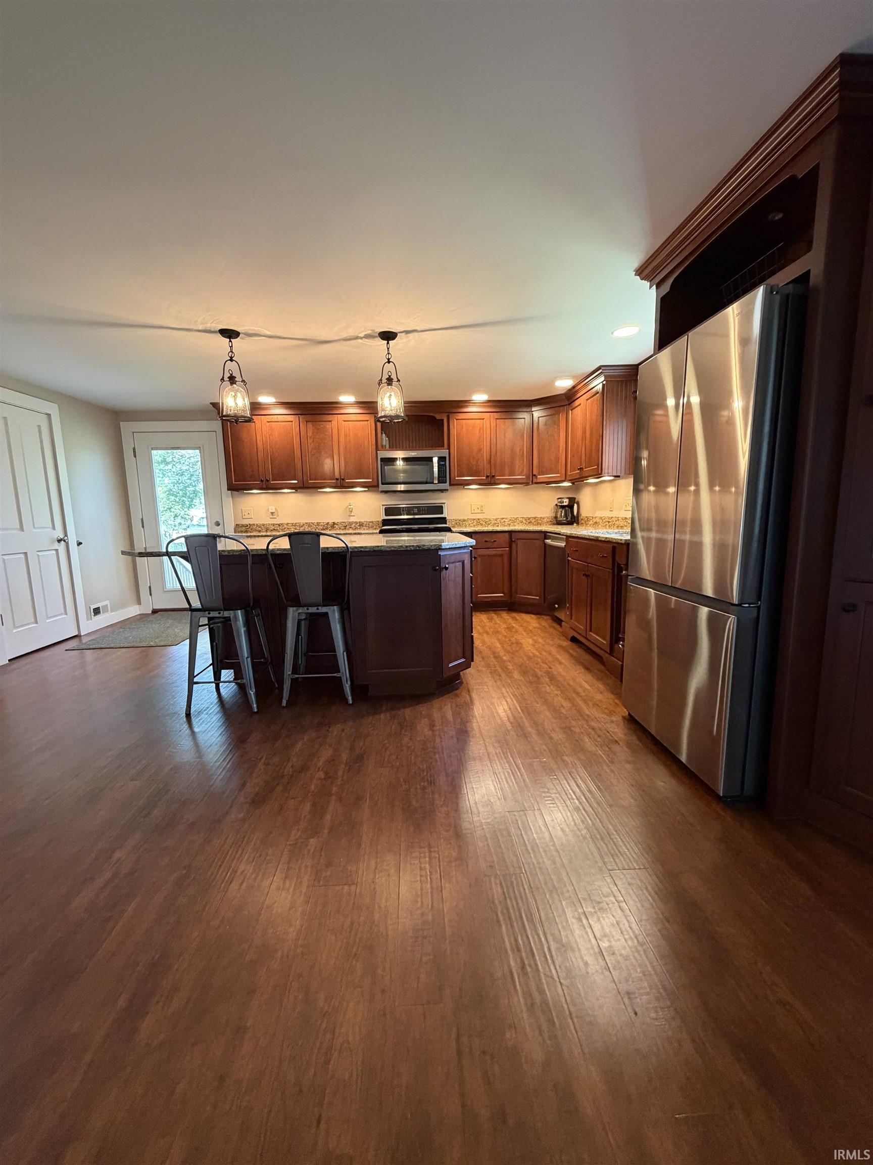 Kitchen featuring wood-finish flooring, dark wood cabinetry, a central island with countertop seating, stainless steel appliances, and recessed lighting