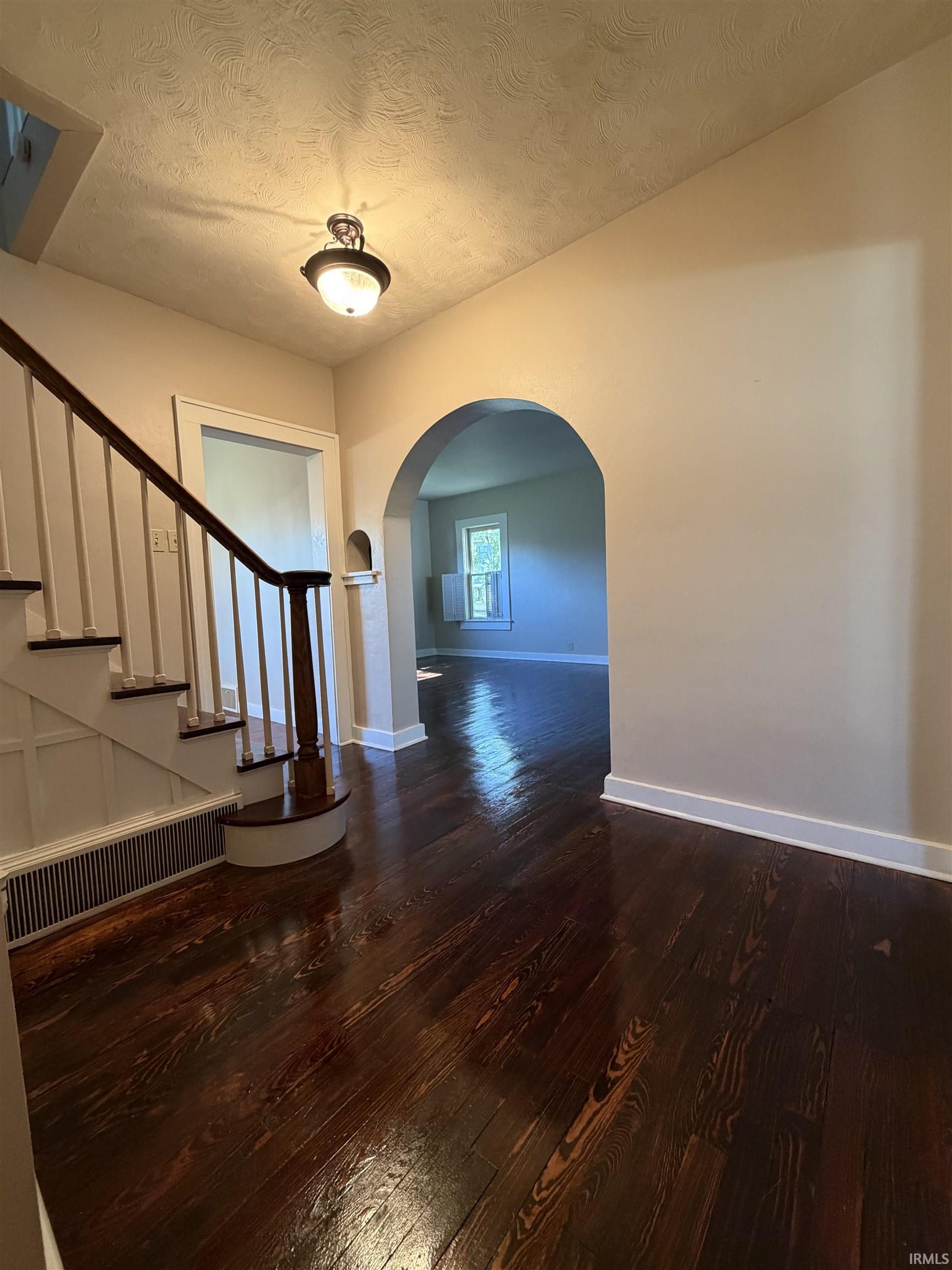 Foyer featuring dark wood-finish flooring, a built-in archway, and a traditional ceiling light fixture