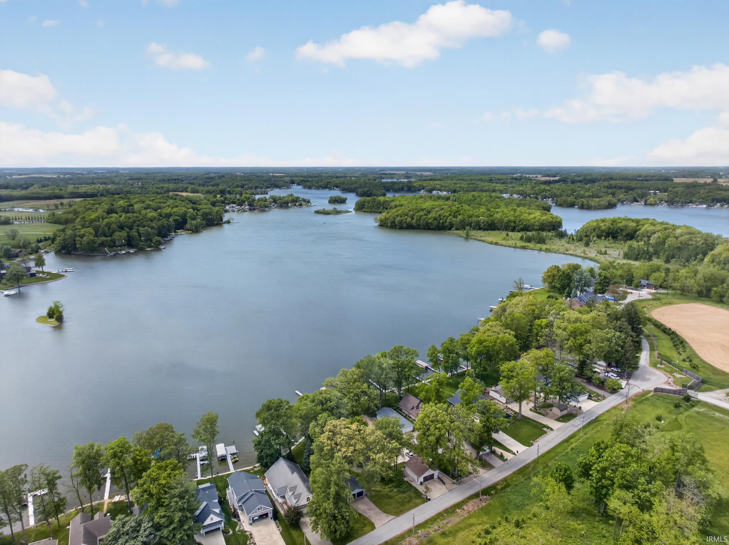 Expansive waterfront setting featuring a tranquil lake, multiple private docks, lush mature trees, and residential properties lining the shore