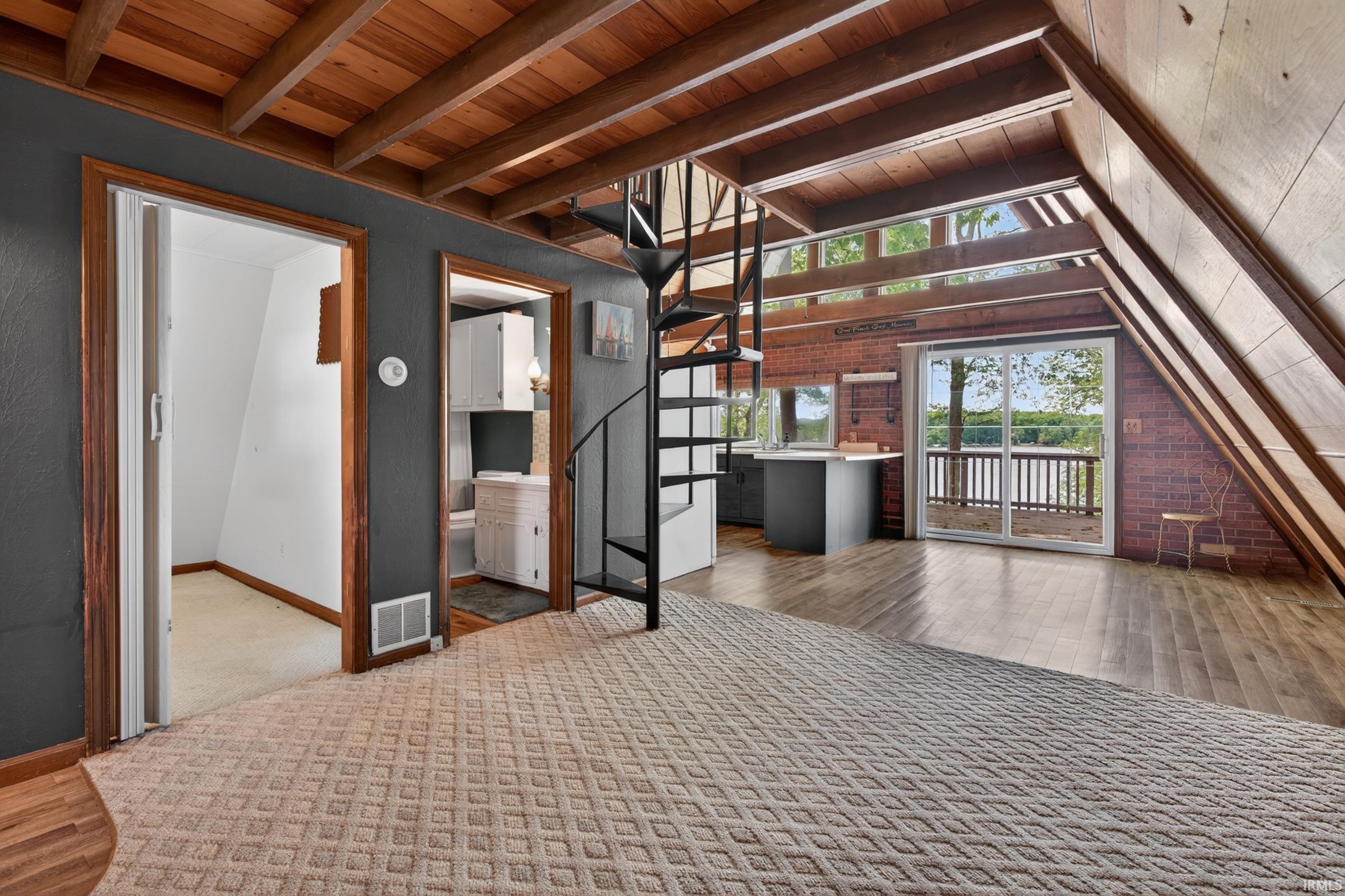 Open living area featuring a spiral staircase, exposed wood beam ceiling, wood-finish flooring, and a sliding glass door opening to a balcony with water
