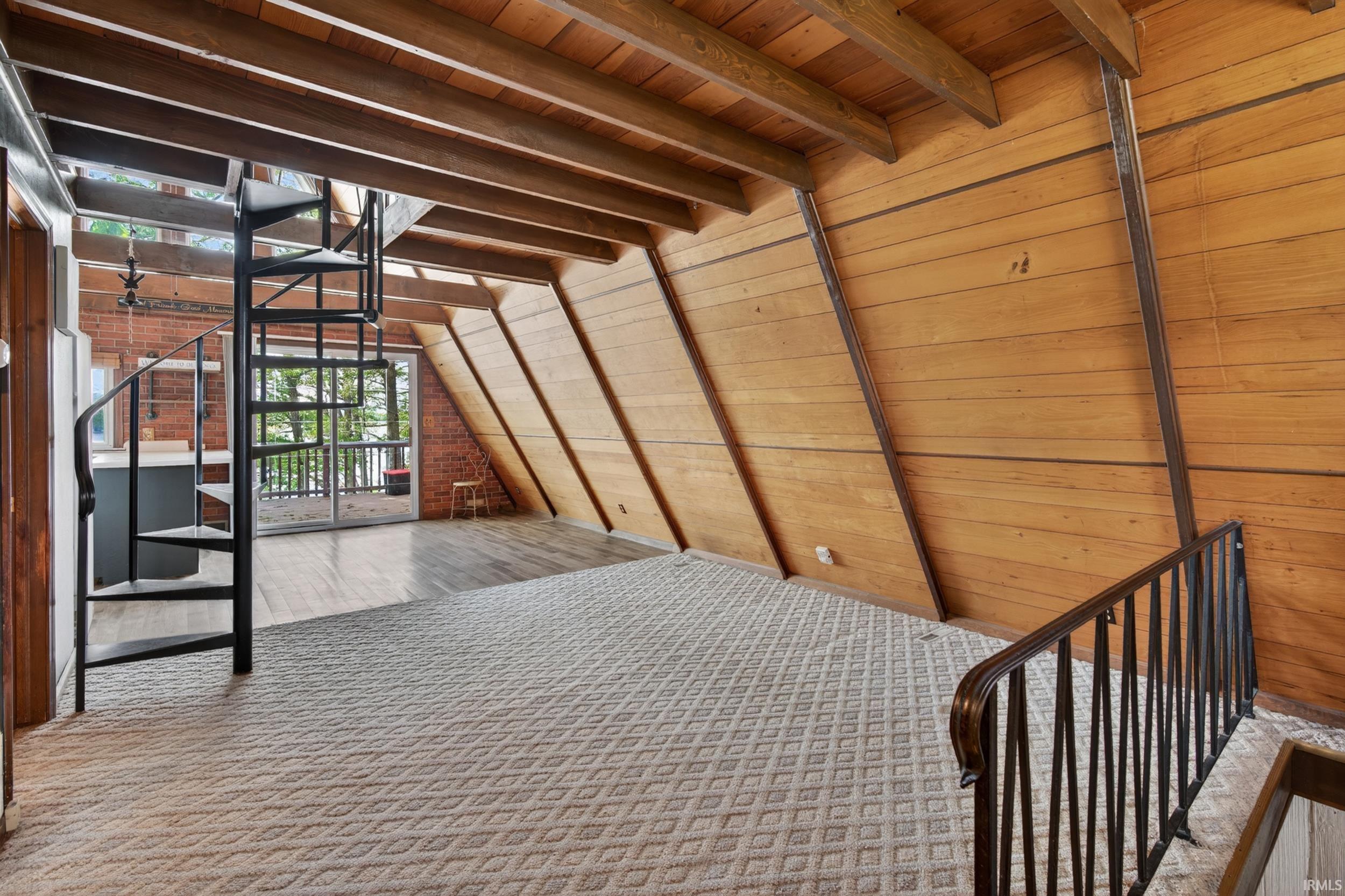 Loft space featuring a black spiral staircase, exposed wood beam ceiling, and horizontal wood-paneled walls