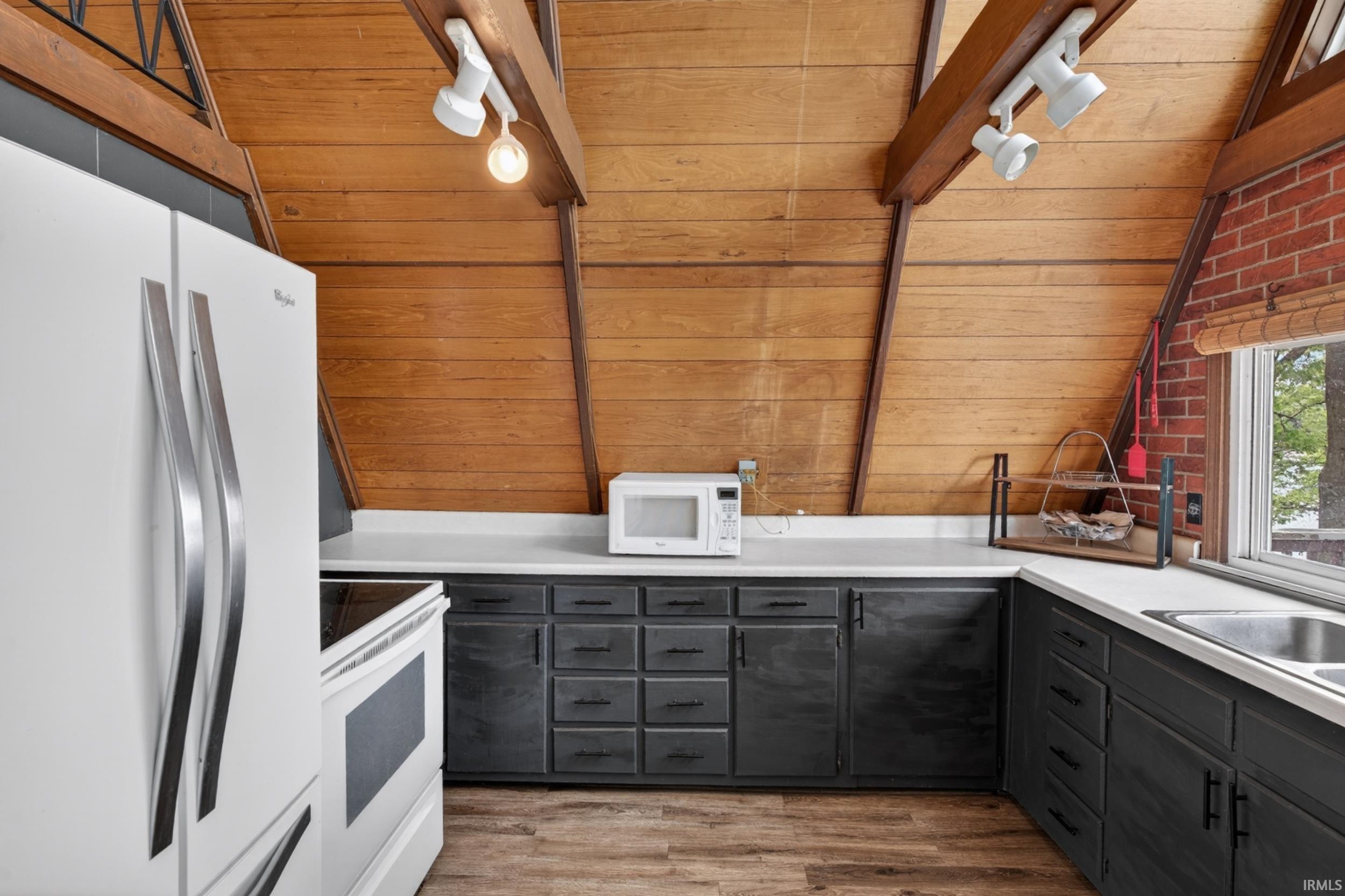 Kitchen featuring wood-finish vaulted ceilings, exposed ceiling beams, white countertops, dark cabinetry with dark hardware, and a stainless steel sink