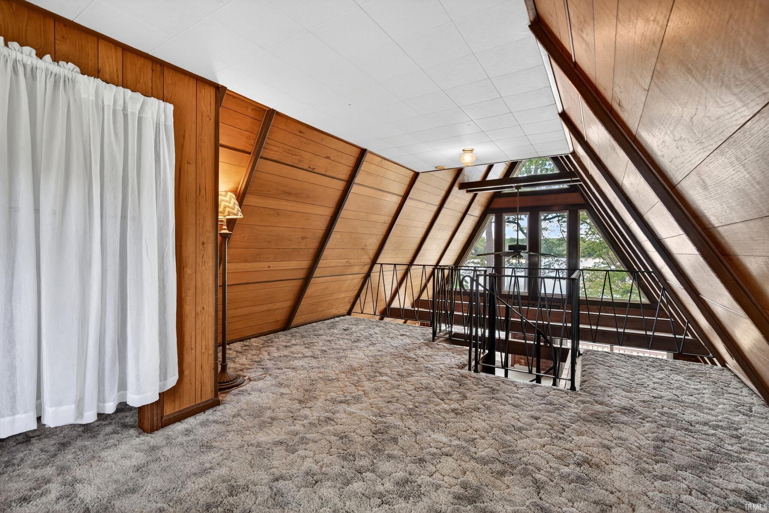 A-frame interior featuring wood-paneled walls, vaulted ceiling with white acoustic panels, and grey shag carpeting
