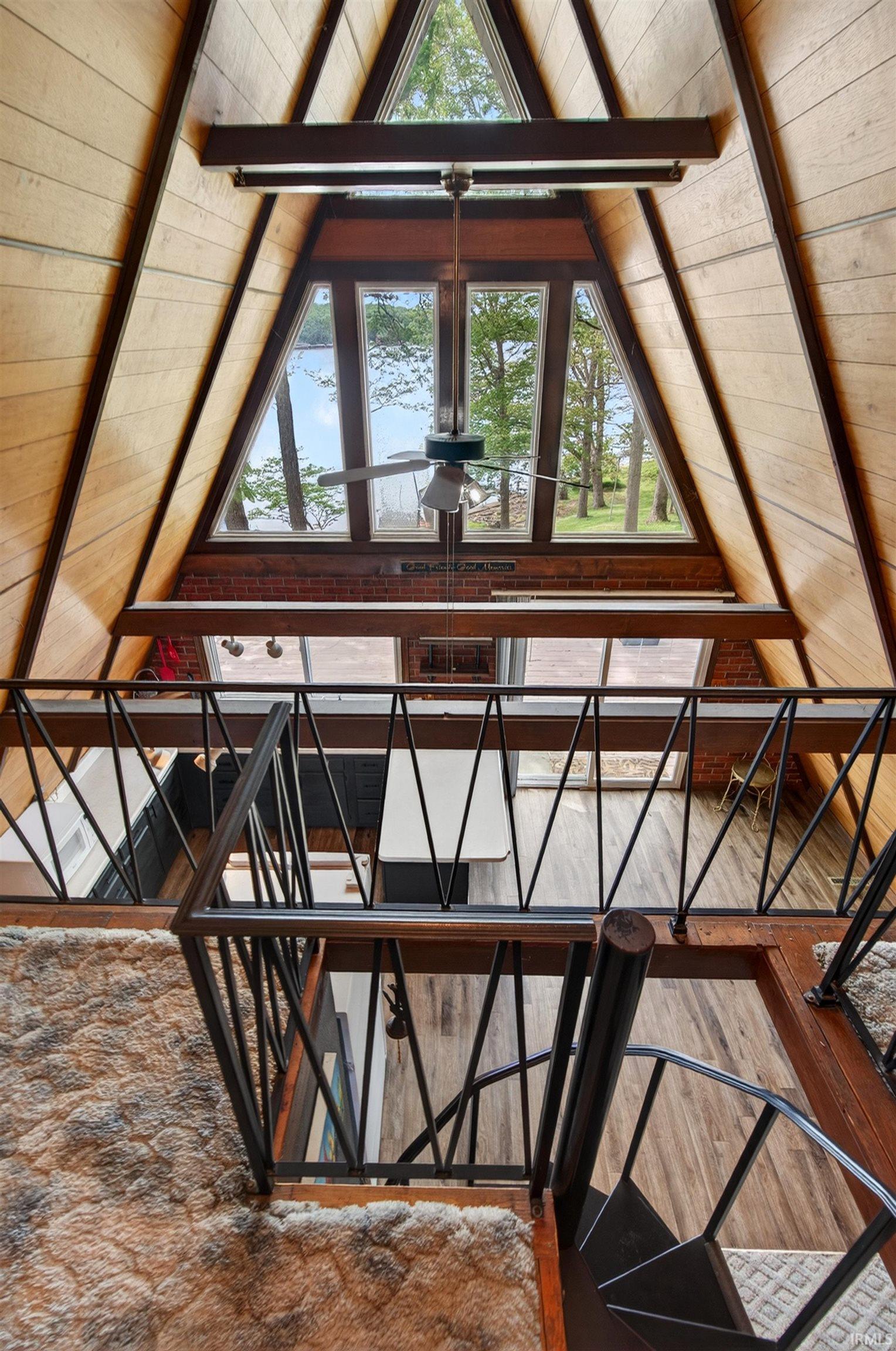 Open-concept living space with expansive A-frame windows, wood-finish wall paneling, and exposed beam ceiling