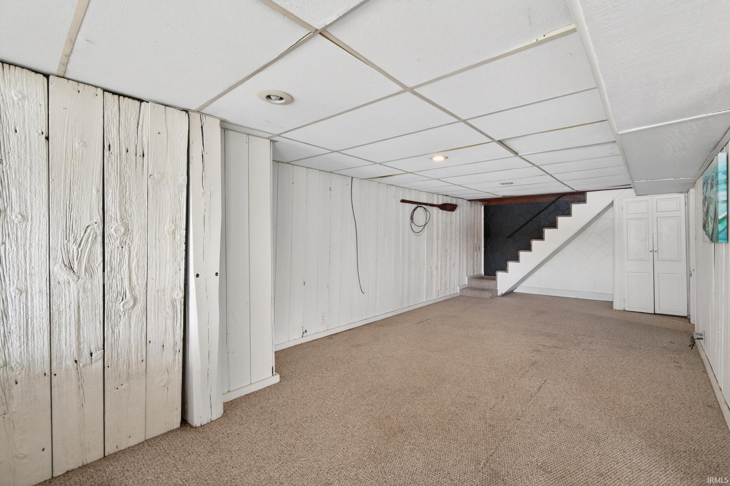 Carpeted lower-level room featuring white plank paneling and a drop ceiling with recessed lighting
