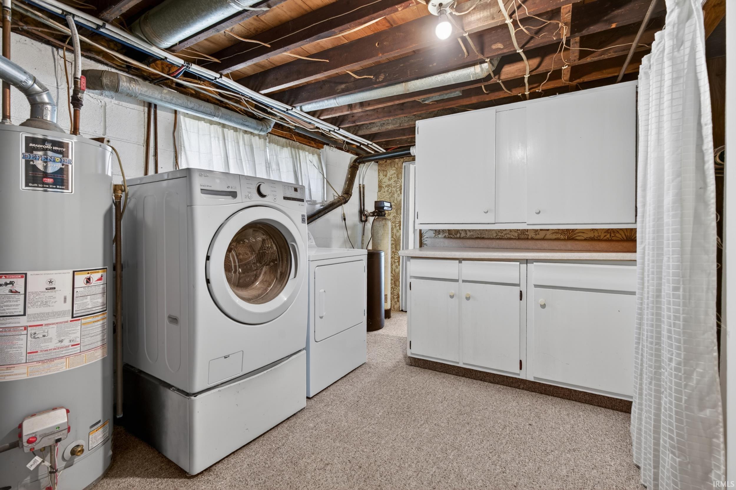 Laundry area featuring a front-loading washer and dryer set, water heater, and built-in white cabinetry with countertop space