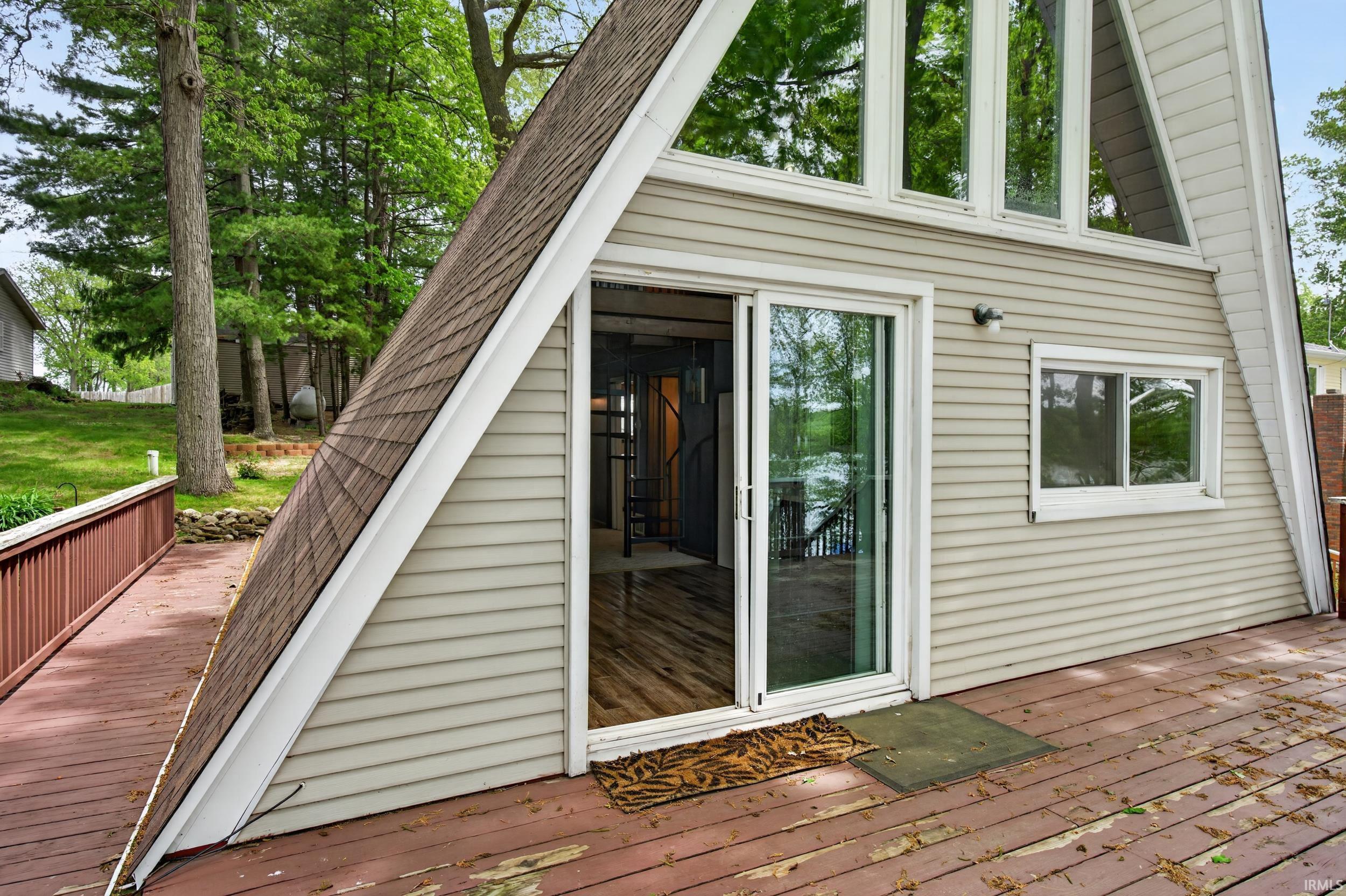 A-frame exterior featuring horizontal siding, a shingle roof, expansive deck, full-light sliding door, and upper-level transom windows