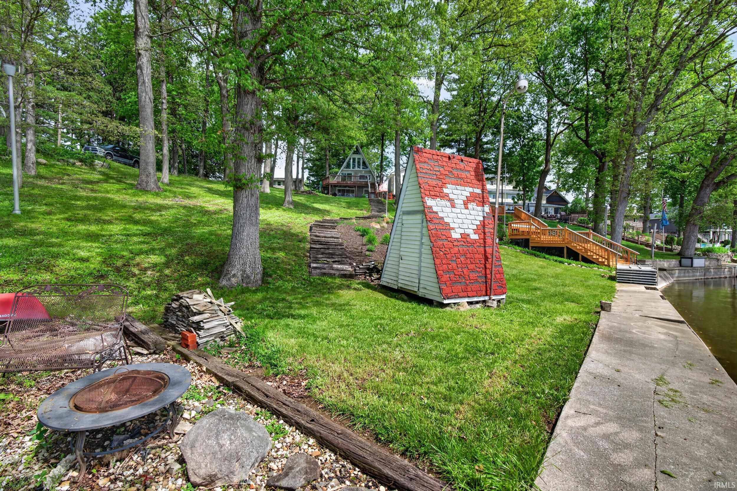 Lakeside property featuring a concrete seawall, sloped grassy terrain with mature trees, and a wooden staircase leading to upper levels