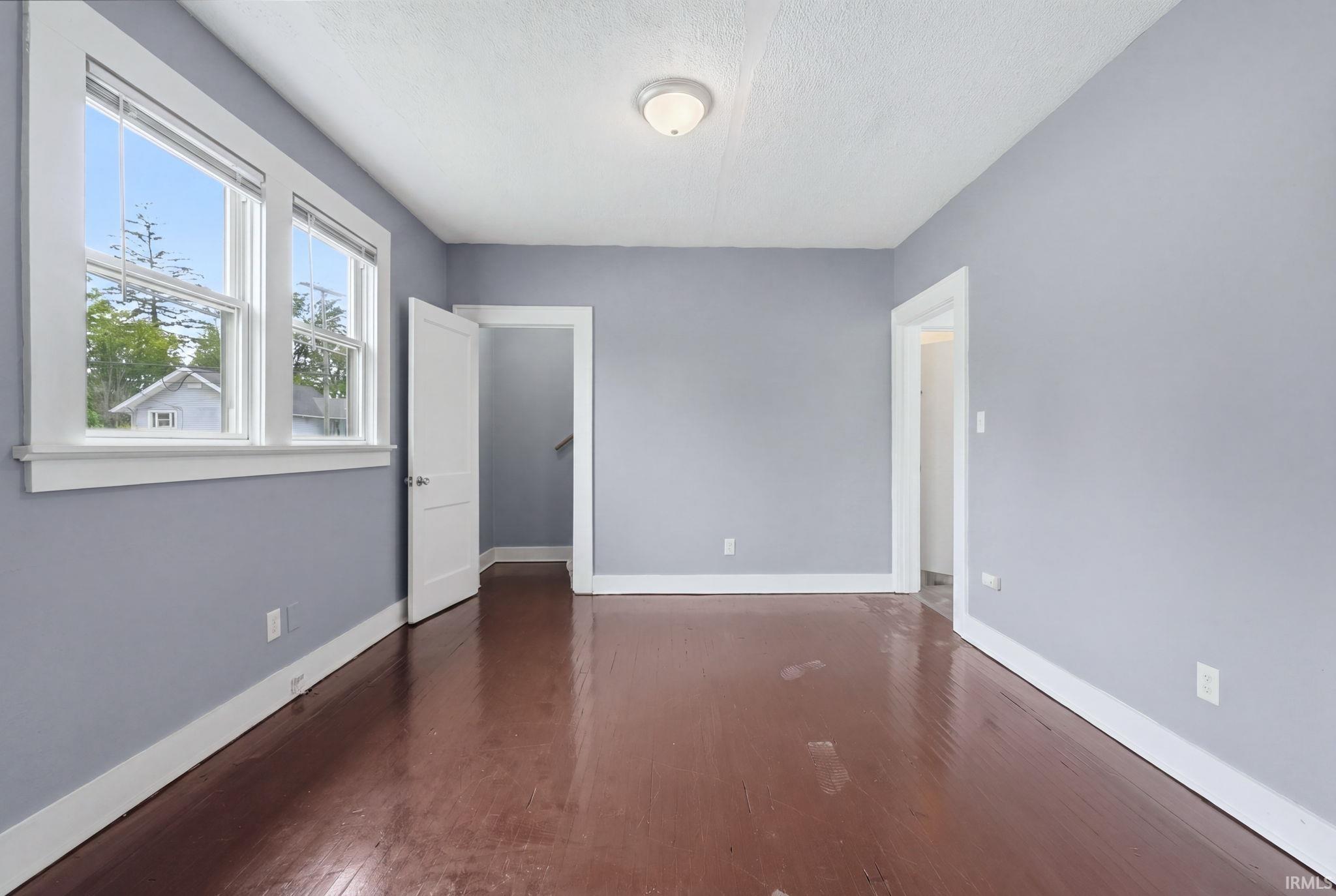 Room featuring two windows with white trim, wood-finish flooring, light blue wall paint, and white baseboards