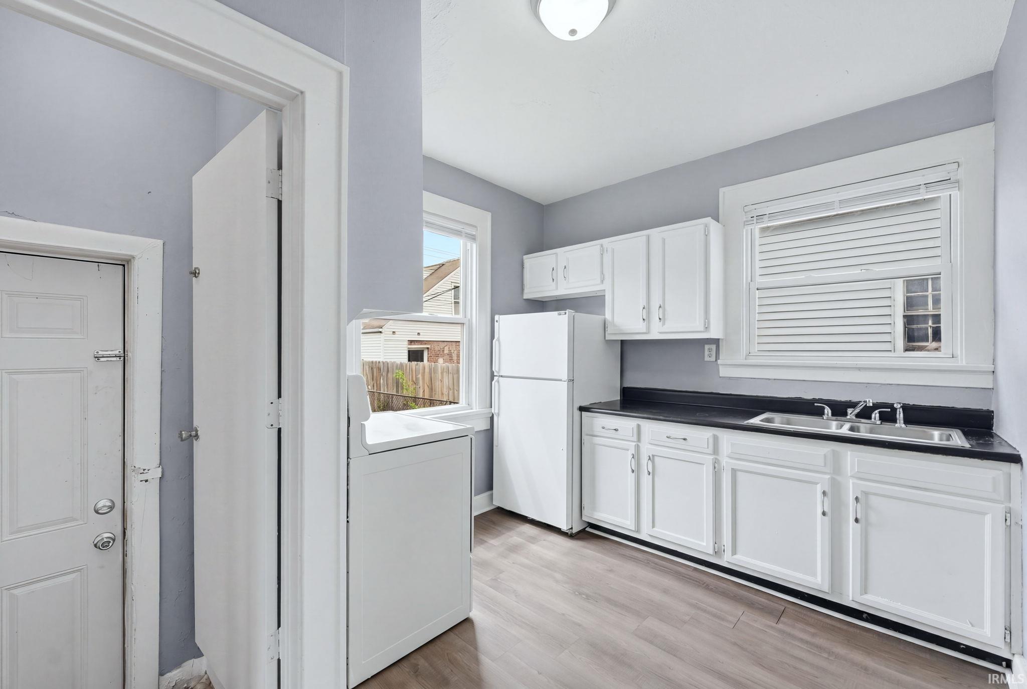 Kitchen featuring white cabinetry, dark countertops, a double basin stainless steel sink, and wood-finish flooring