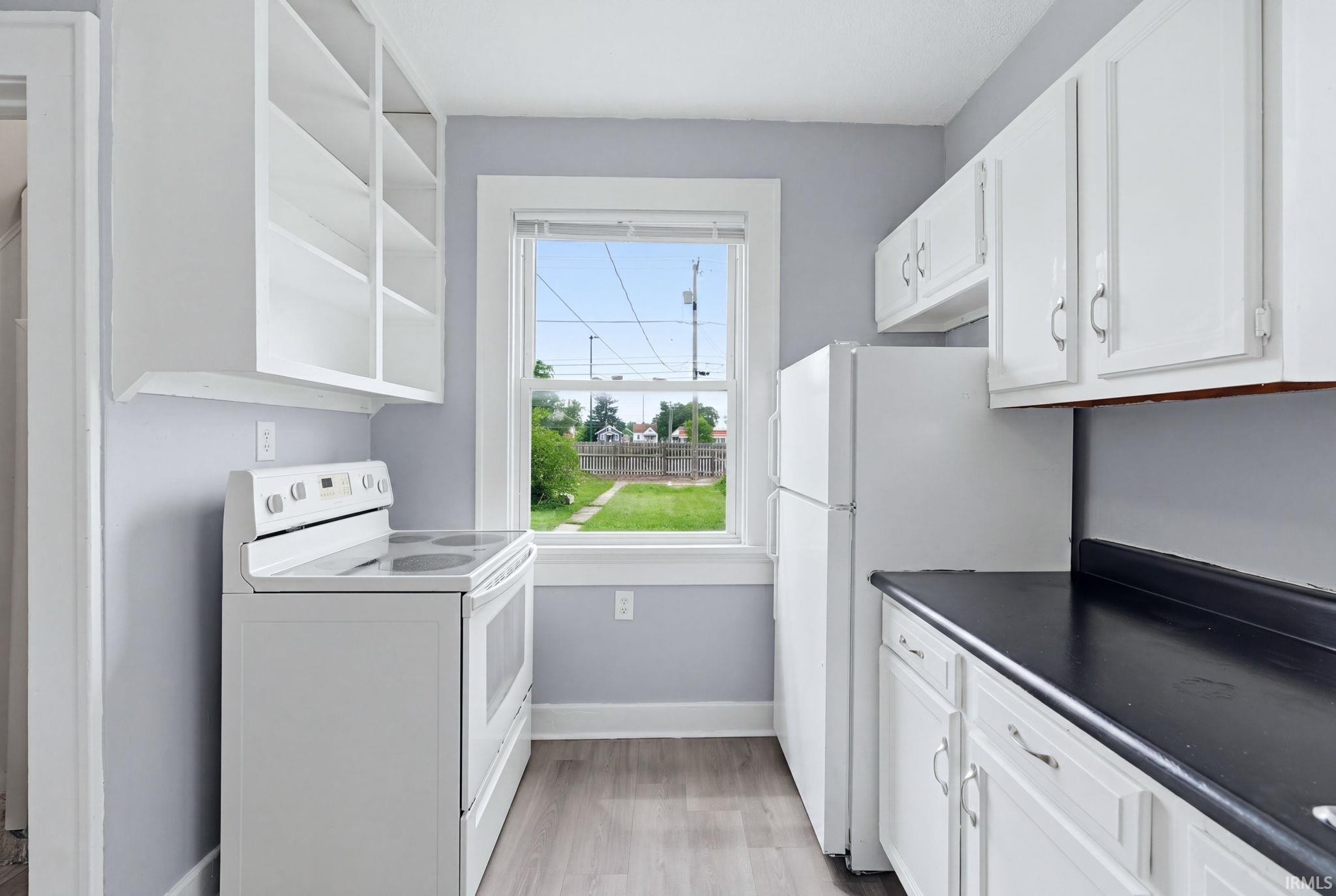 Kitchen featuring white cabinetry, a white electric range, a white refrigerator, black countertops, and wood-finish flooring