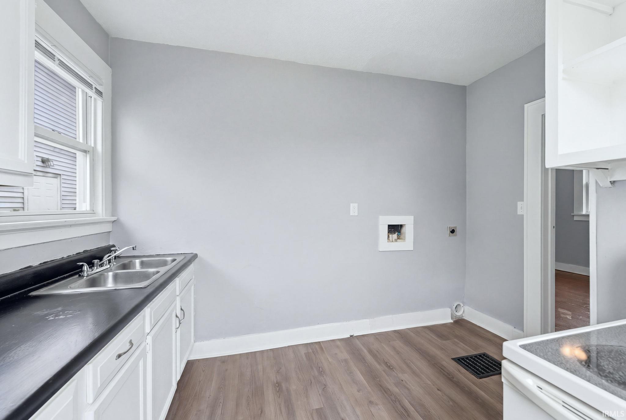 Kitchen area featuring wood-finish flooring, light gray walls, white base cabinetry, and a double basin stainless steel sink with a dark countertop